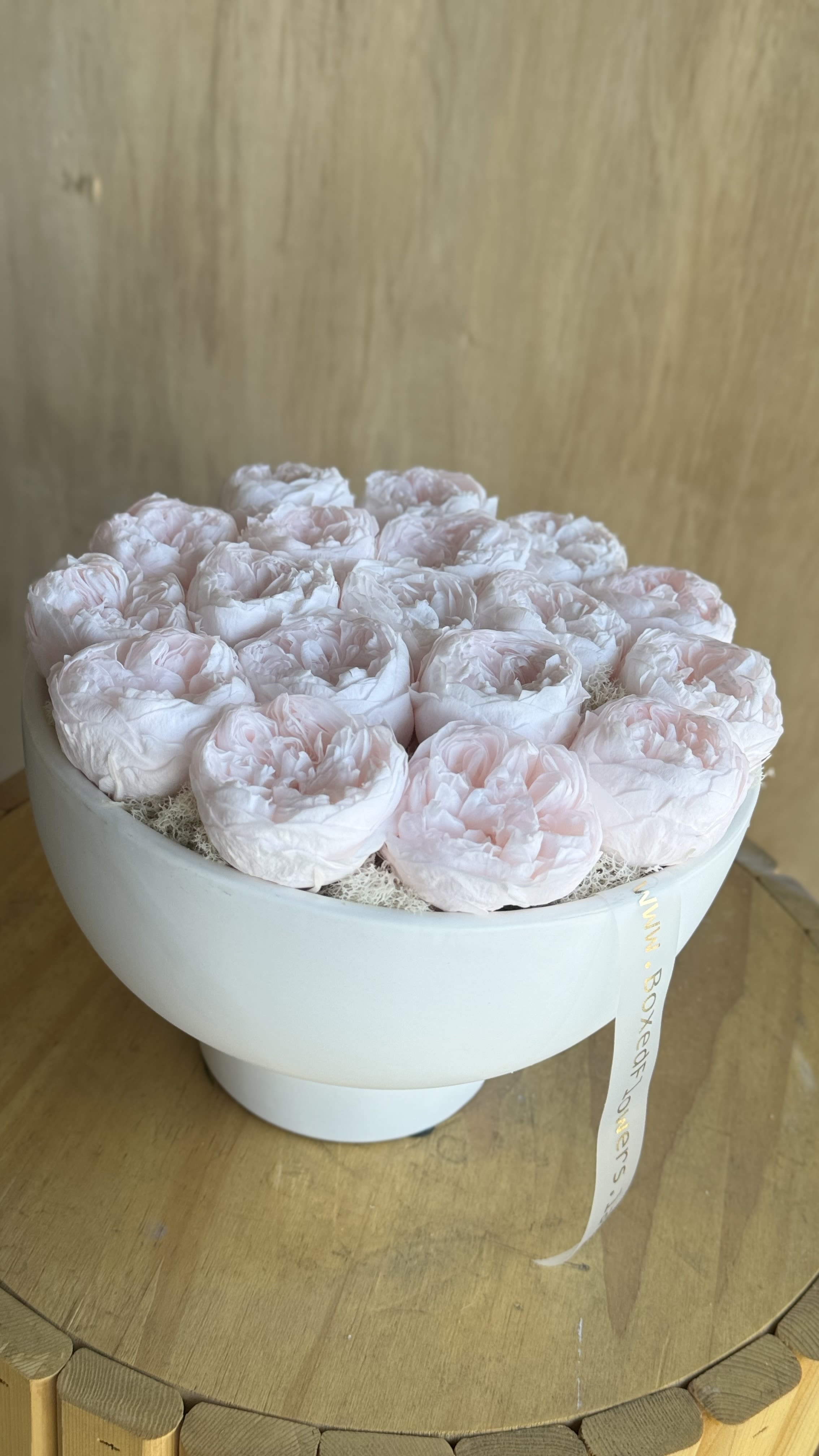 Round box of pale pink peonies with a ribbon tag