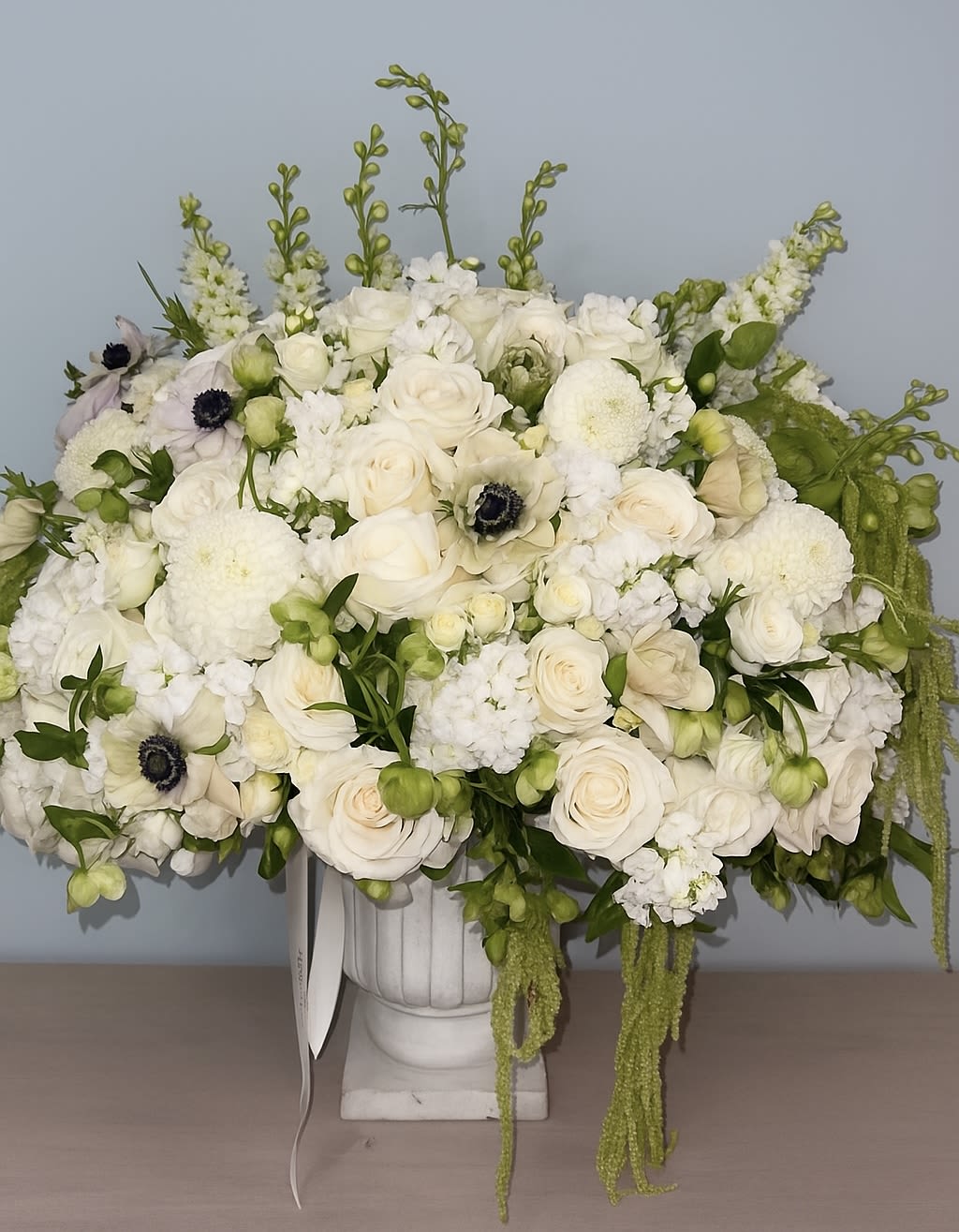 White floral arrangement in a white urn vase with trailing green accents