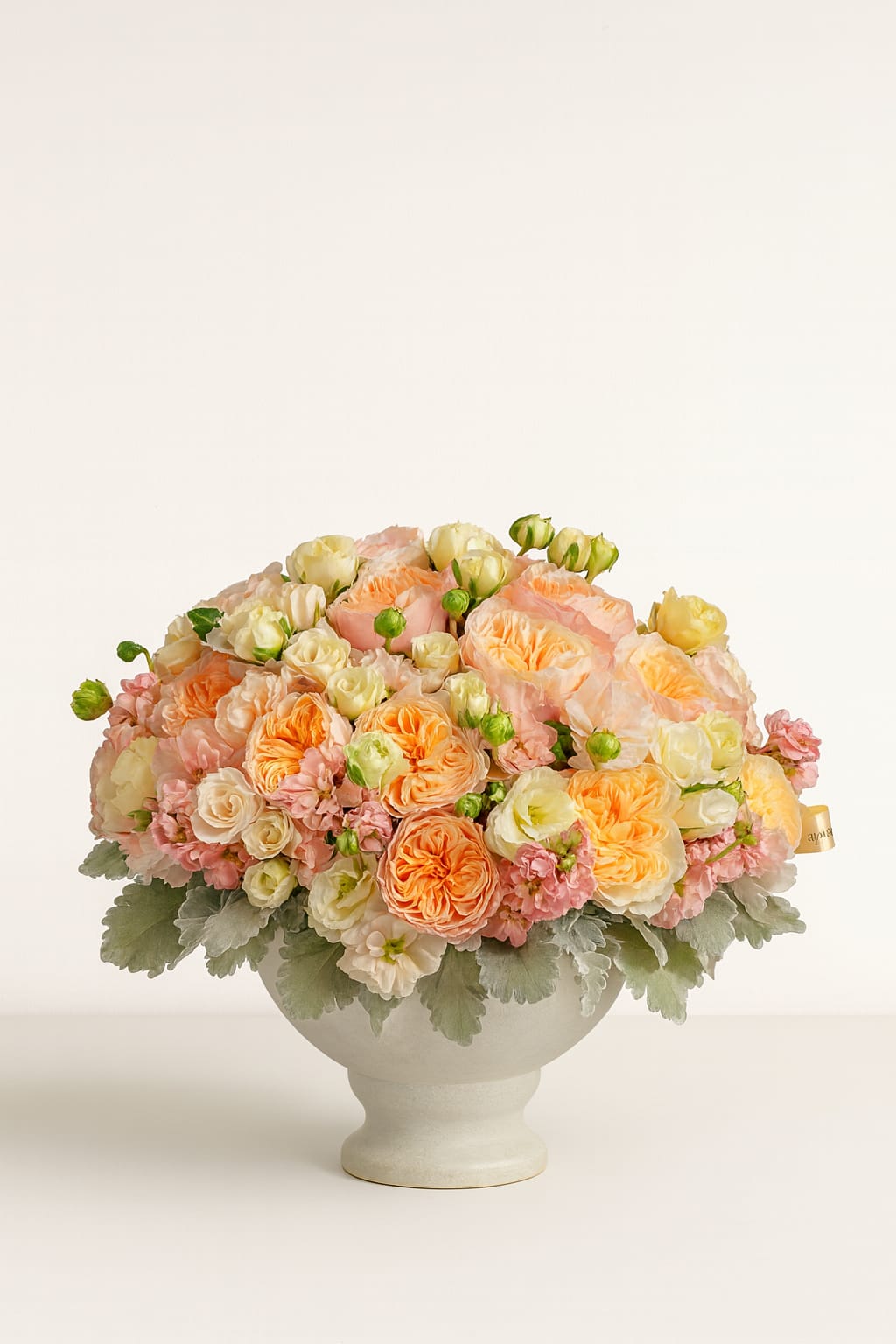 Peach and cream rose arrangement in a white pedestal vase