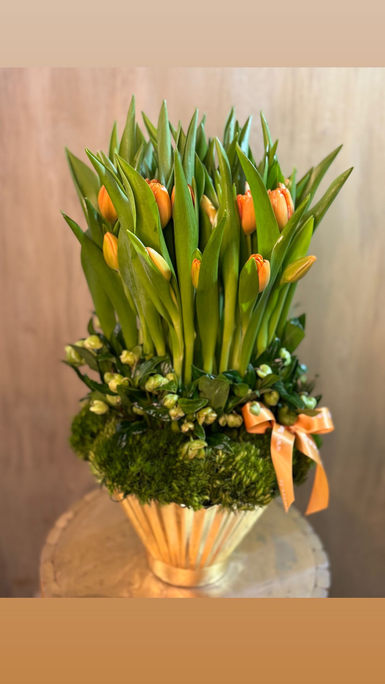 Orange tulips arranged in a gold vase with a ribbon
