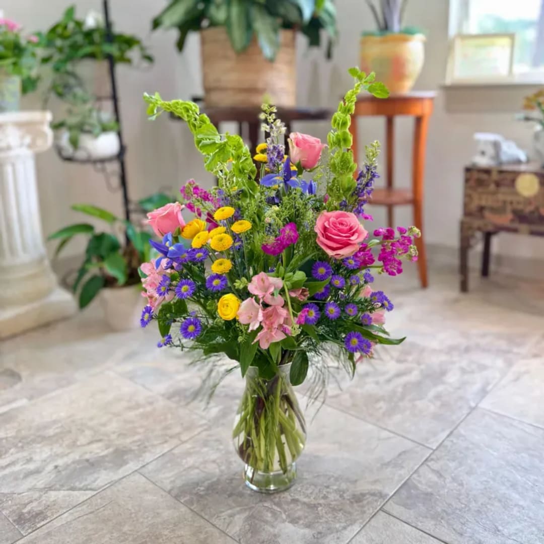 Mixed bouquet of pink roses, purple daisies, and yellow blooms in a glass vase