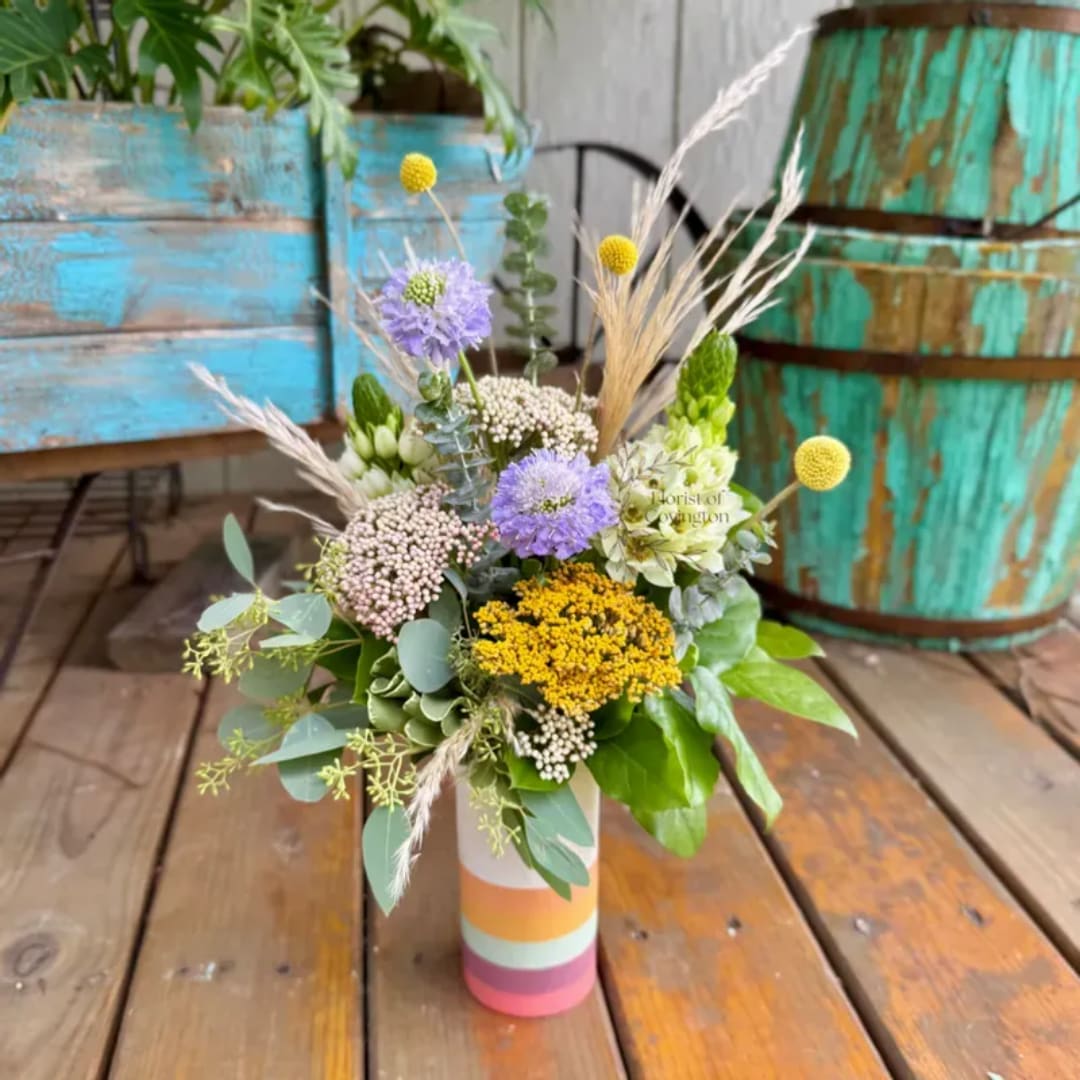 Mixed wildflower bouquet in a striped vase on a wooden table