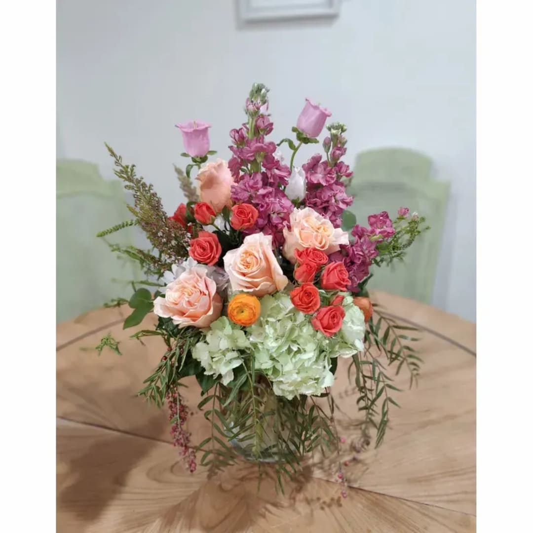 Mixed bouquet of pink, peach, and coral flowers in a clear glass vase
