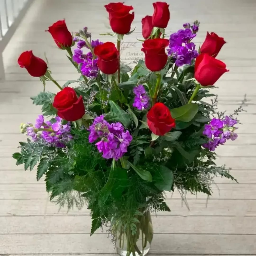 Tall bouquet of red roses and purple flowers in a clear glass vase
