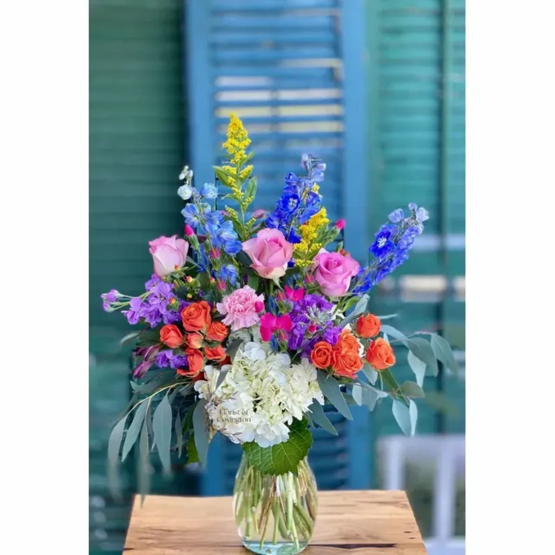 Colorful mixed bouquet in a clear glass vase with pink roses and blue flowers