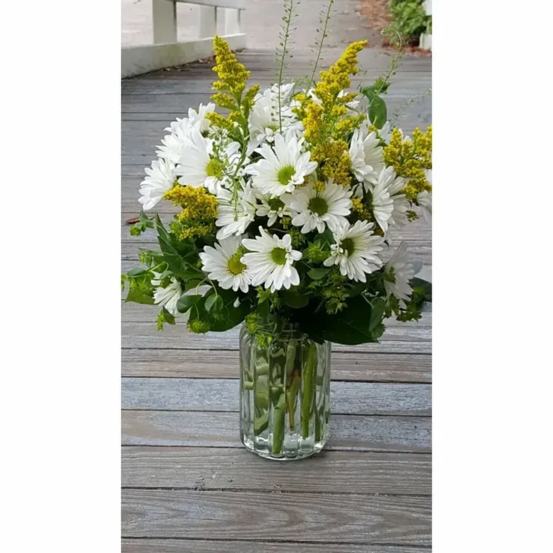 White daisy bouquet with yellow filler in a clear glass vase