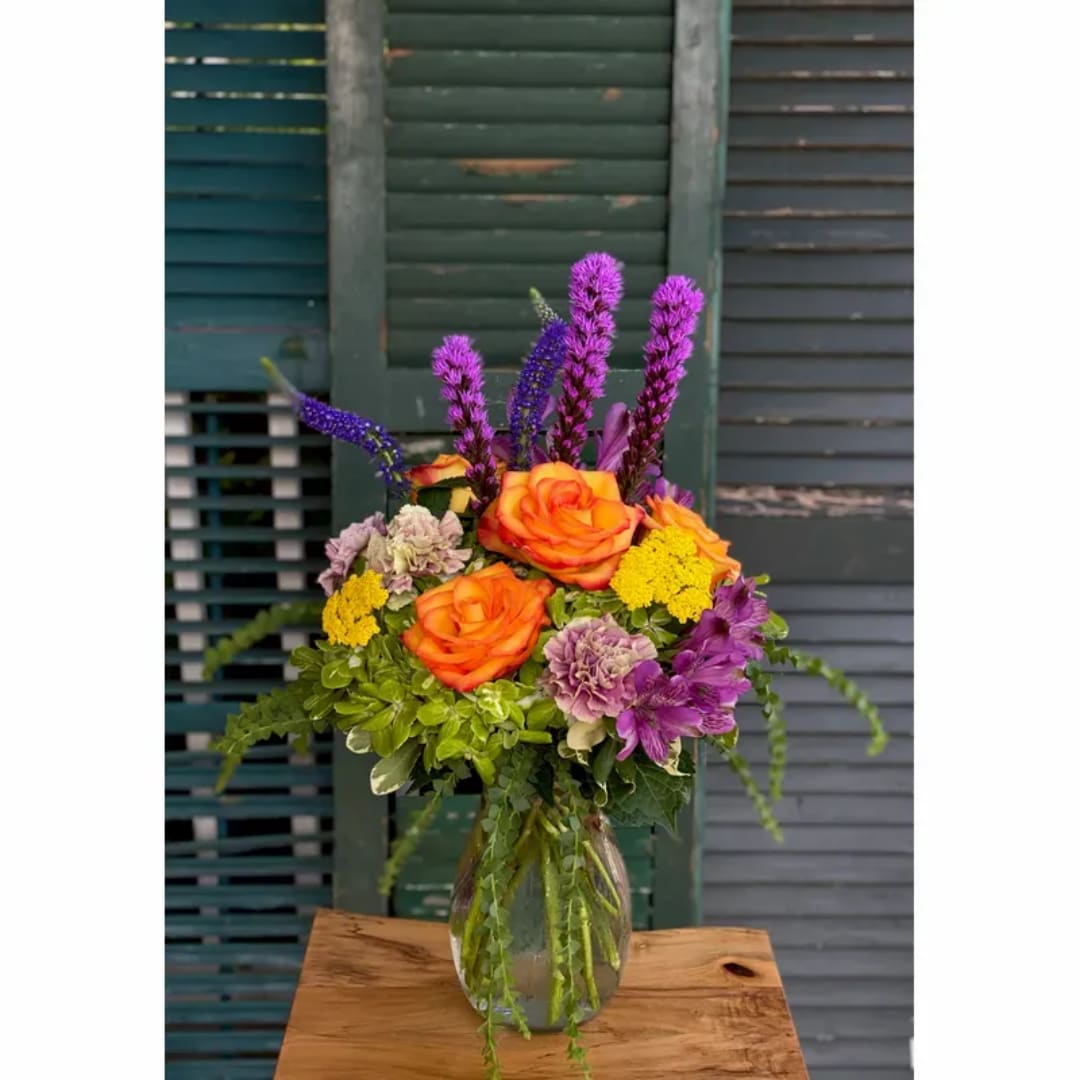 Orange roses and purple flowers in a clear glass vase