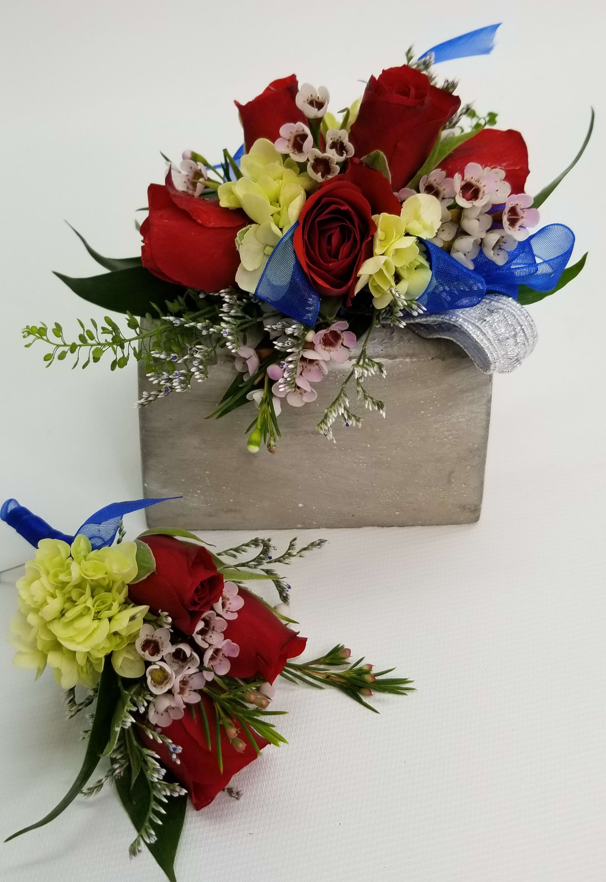 Red and Blue Corsage and Bout set - Red roses, pink wax flower, lime hydrangea, greens, Royal blue ribbon and standard elastic wristlet. Wrist corsage and boutonniere set. 