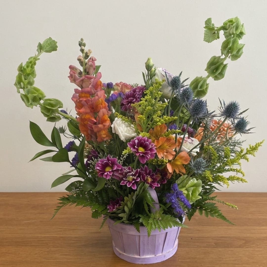 Mixed flower arrangement in a lavender basket with tall green accents