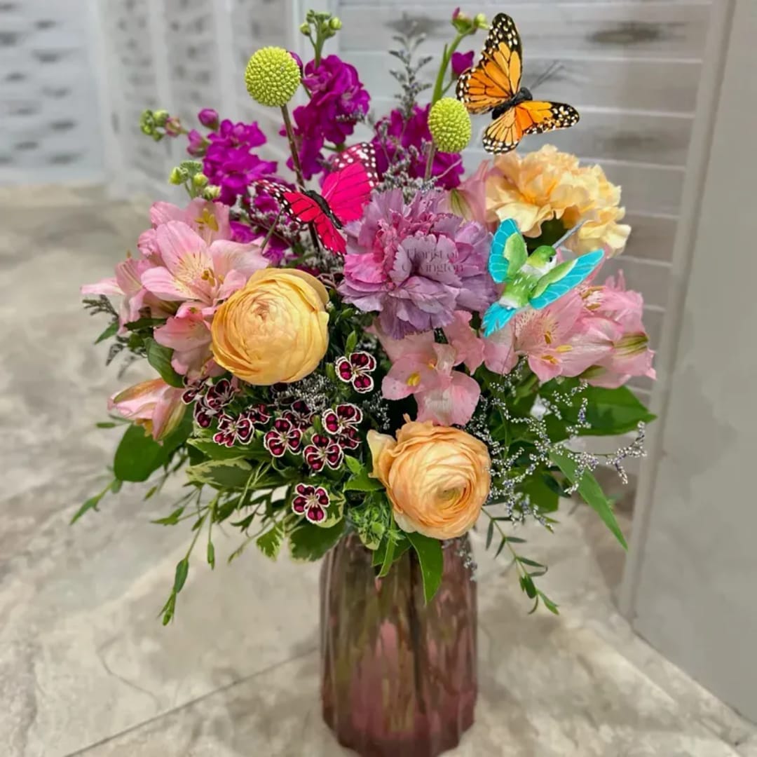 Mixed bouquet in a tall vase with pink, purple, and peach flowers and butterfly picks