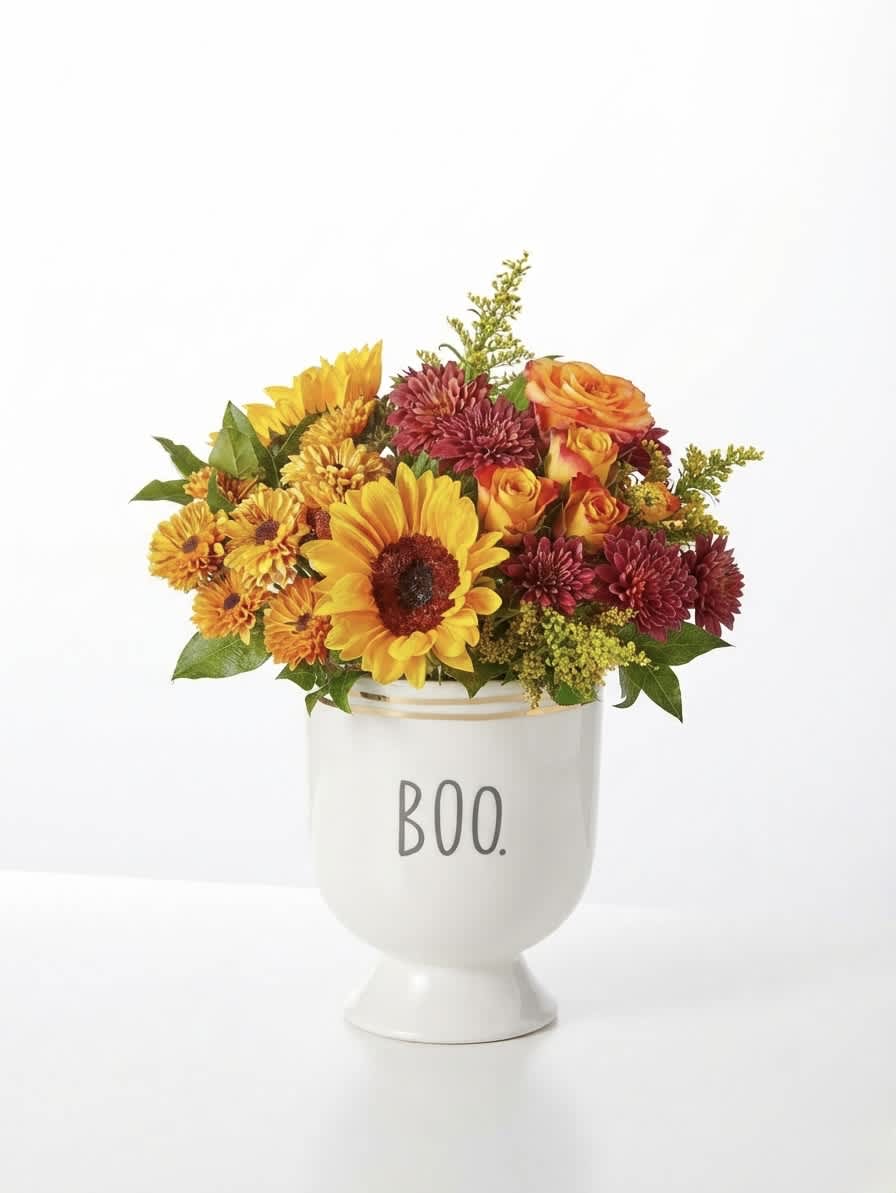 Mixed orange, yellow, and burgundy flowers in a white vase labeled BOO.