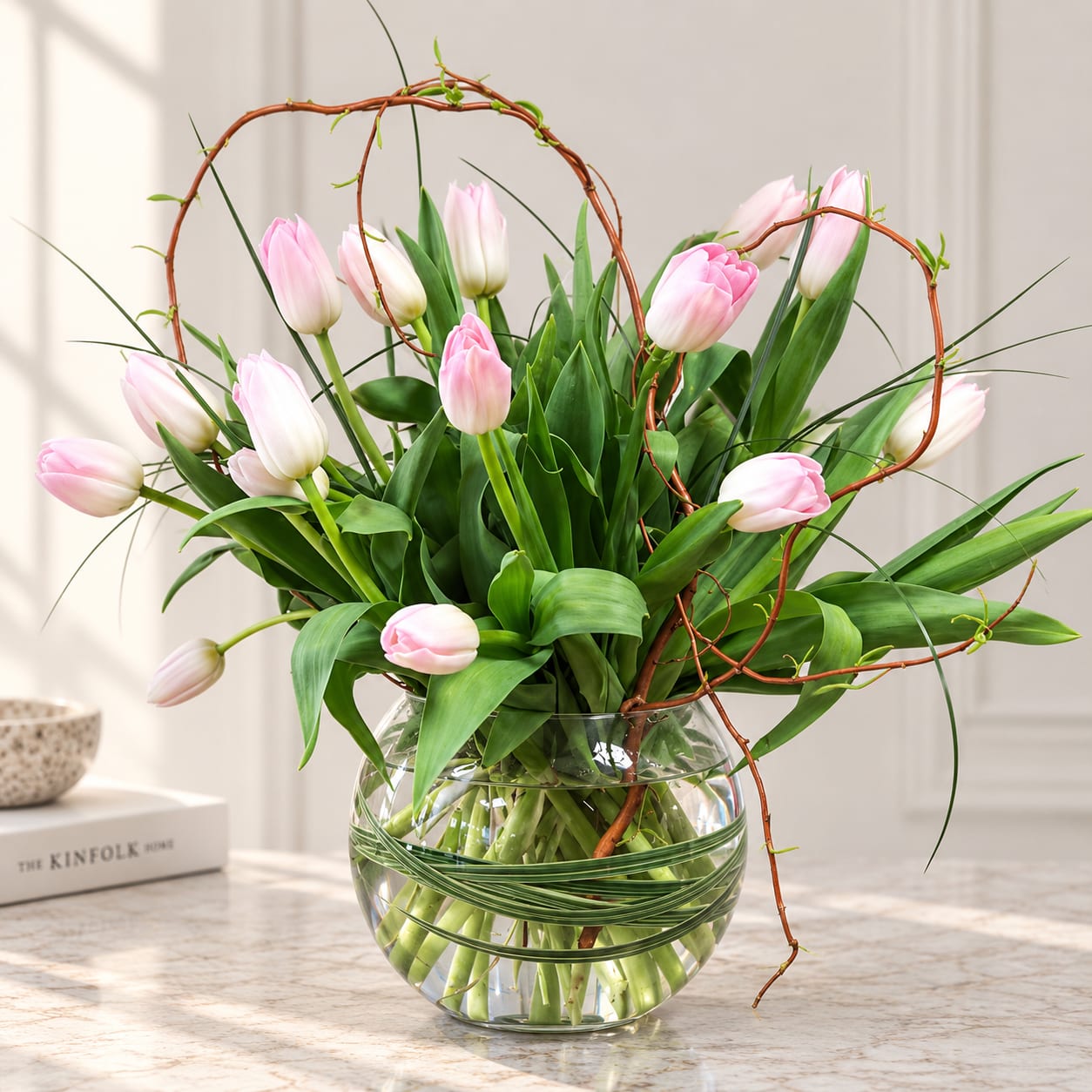 Pink tulips arranged in a clear glass bowl vase with curly branches