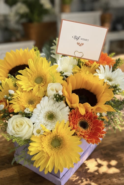 YOU DESERVE THE BEST - A vibrant square box bursting with sunflowers, yellow and orange gerberas, white roses, and white chrysanthemums. 