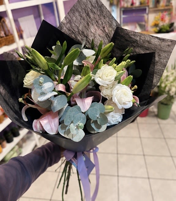 TODAY IS YOUR DAY - A contemporary bouquet of white lisianthus, pink lily buds, and delicate orchid blooms with bold eucalyptus, wrapped in dramatic matte black paper and tied with a lilac ribbon. Sleek, artistic, and unforgettable.