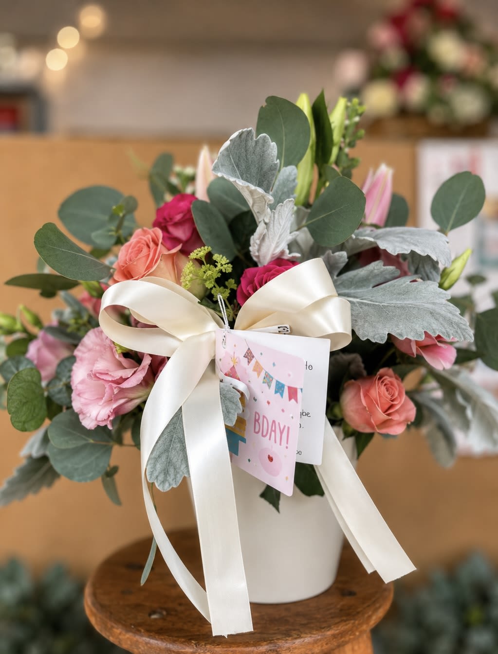 JUST FOR YOU - The ultimate ready-to-give birthday gift — this stunning ceramic vase arrangement is packed with peach roses, hot pink spray roses, blush lisianthus, soft pink lily buds, silvery dusty miller, and fresh eucalyptus, finished with a gorgeous oversized cream satin bow and a personalized gift tag. The lily buds open over several days, meaning the lucky recipient gets to enjoy a bouquet that literally keeps blooming all week long. The white ceramic vase is theirs to keep — a lasting reminder of your thoughtfulness. No wrapping, no extras needed. Just pure, beautiful joy, ready to deliver.