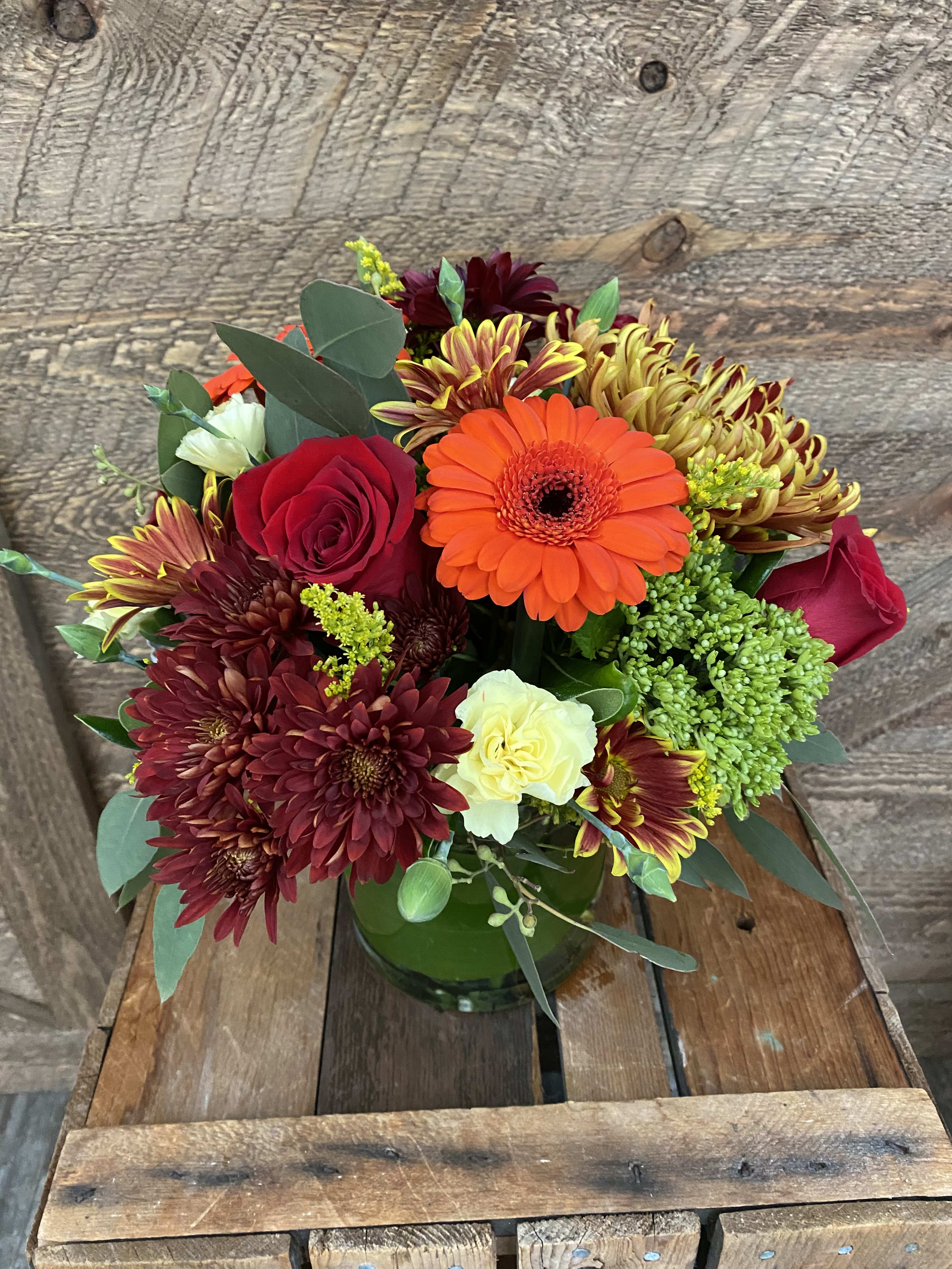 Mixed bouquet of red, orange, and yellow flowers in a green glass vase