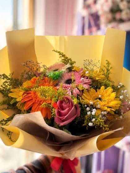 YOU DID IT! - A lively, colorful bouquet of orange, yellow, and pink gerberas, a bold rose, baby's breath, and solidago, wrapped in yellow and kraft paper with a red bow. Fun and festive for any celebration. 