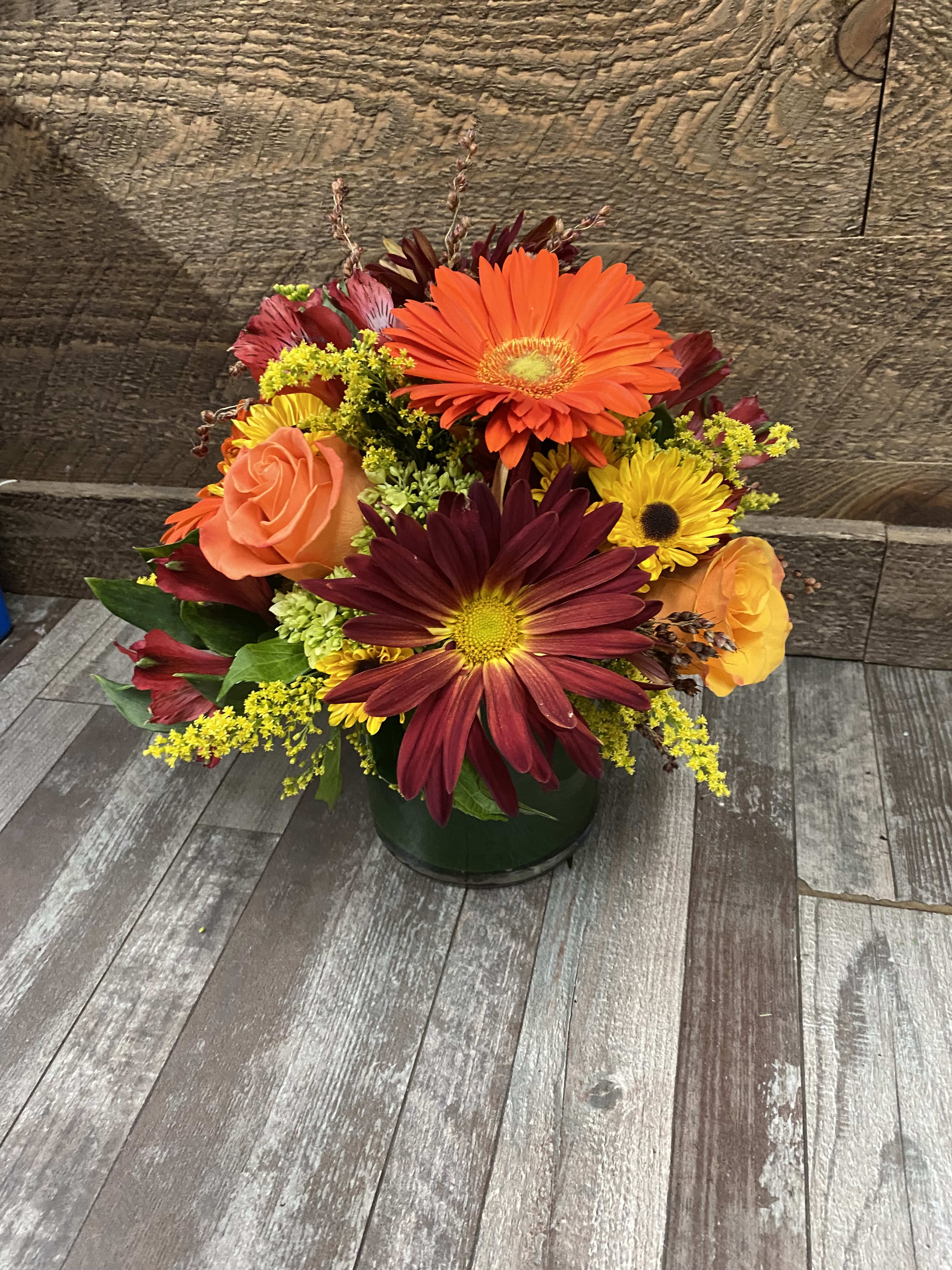 Mixed bouquet of orange, yellow, and burgundy flowers in a dark vase