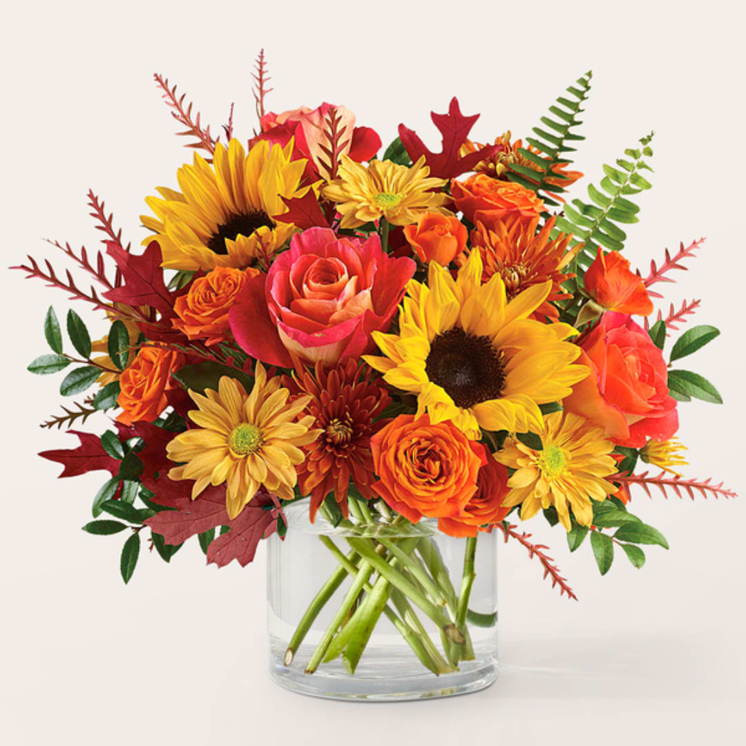 Bouquet of sunflowers, roses, and mums in a clear glass vase