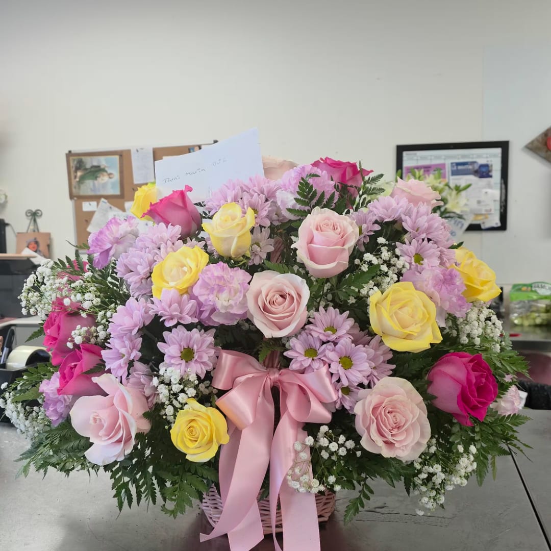Mixed pink, yellow, and lavender flowers in a basket with a pink ribbon