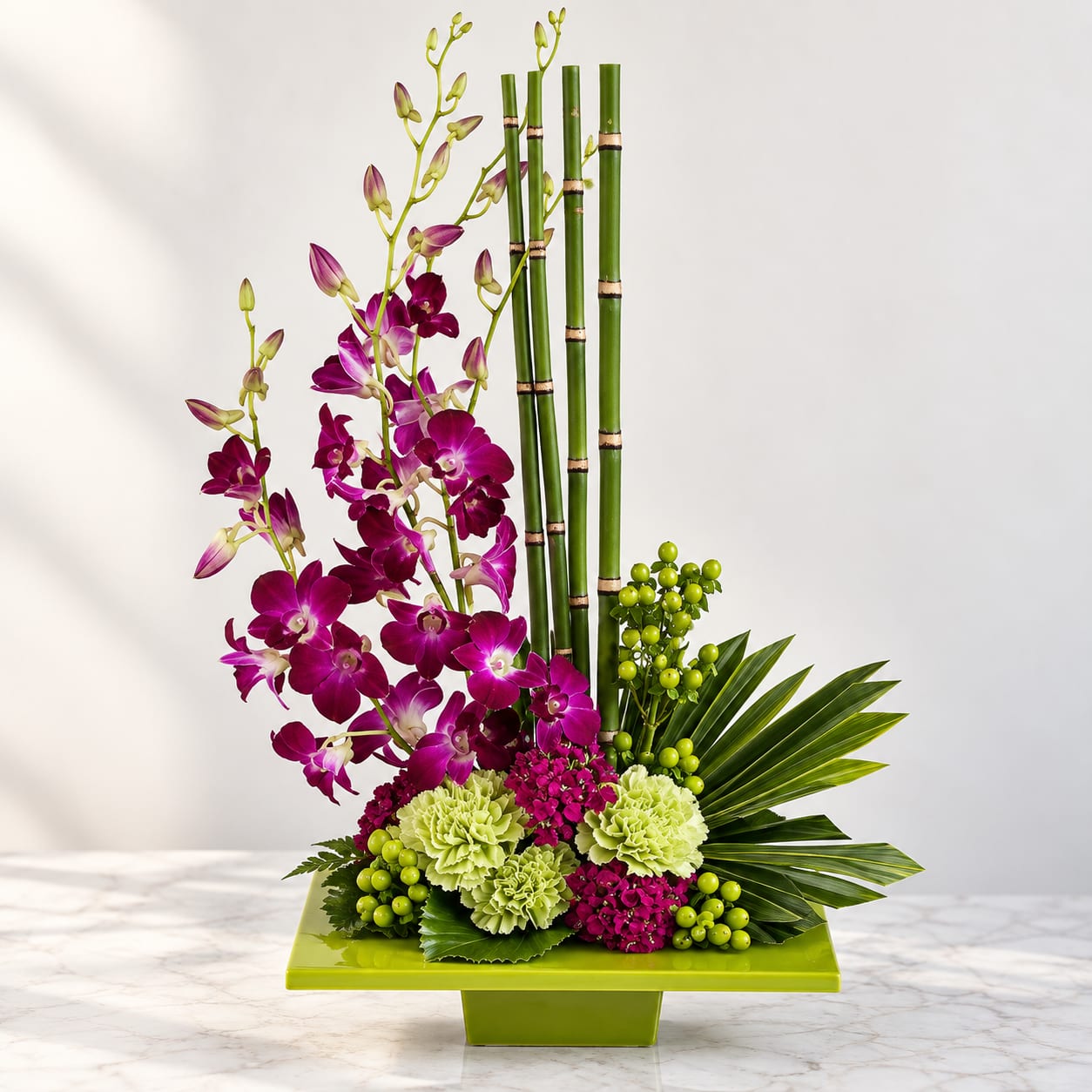 Purple orchids arranged with green carnations and bamboo in a lime vase