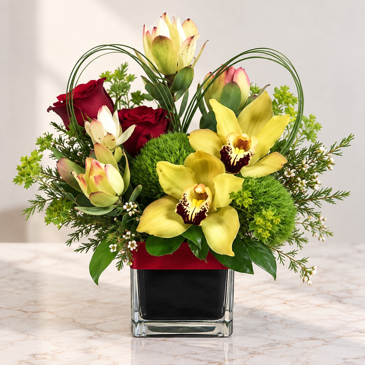 Arrangement of yellow orchids and red roses in a square glass vase