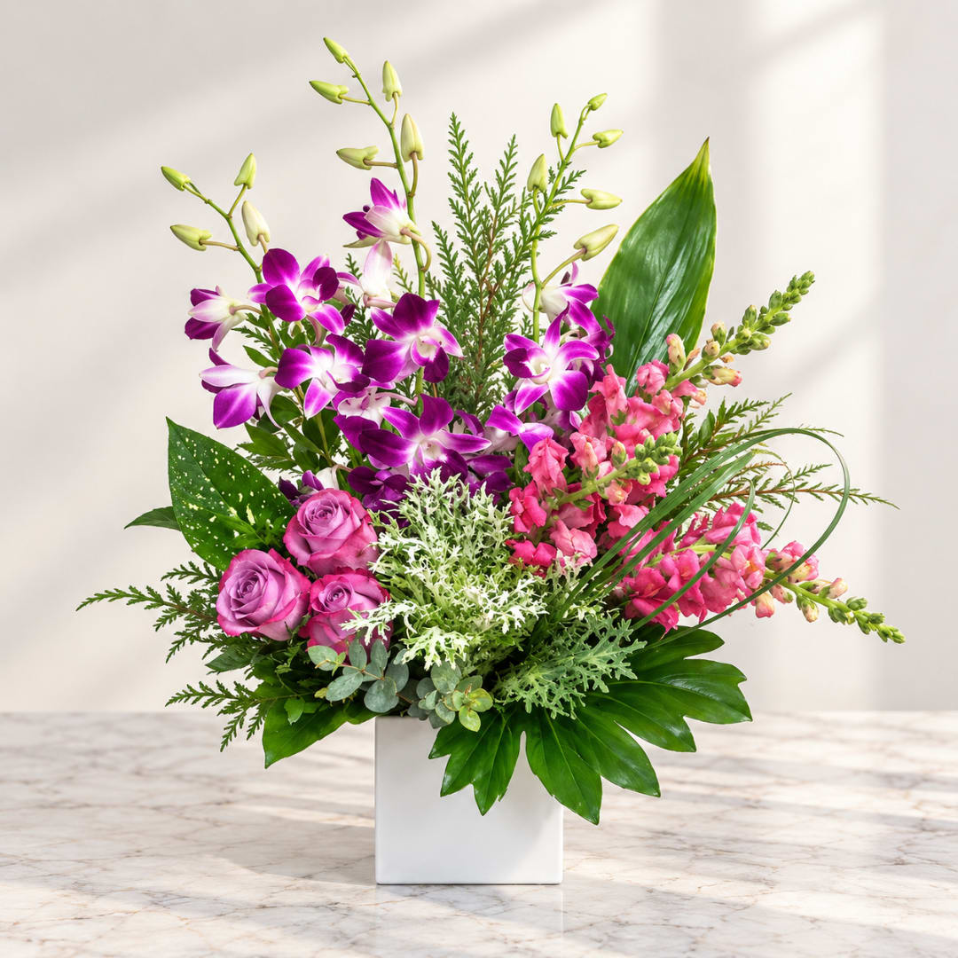 Pink and purple orchid arrangement in a white square vase