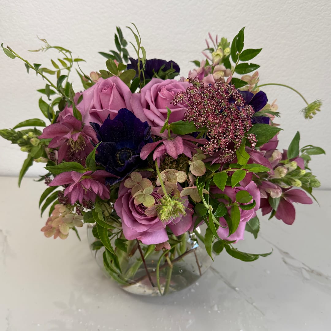 Pink roses and dark purple flowers in a clear glass vase