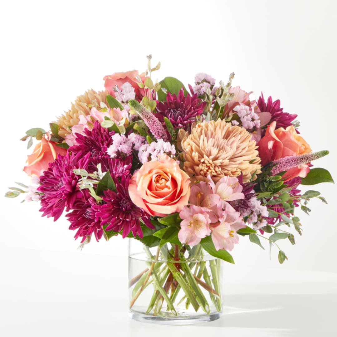 Mixed bouquet of pink, peach, and purple flowers in a clear glass vase