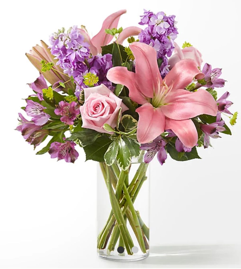 Pink lilies and roses with purple flowers in a clear glass vase