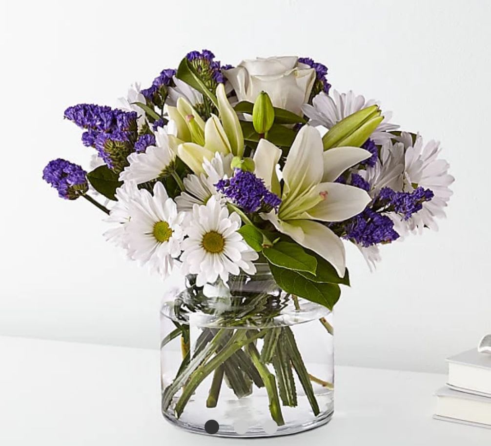 White lilies and daisies with purple filler in a clear glass vase