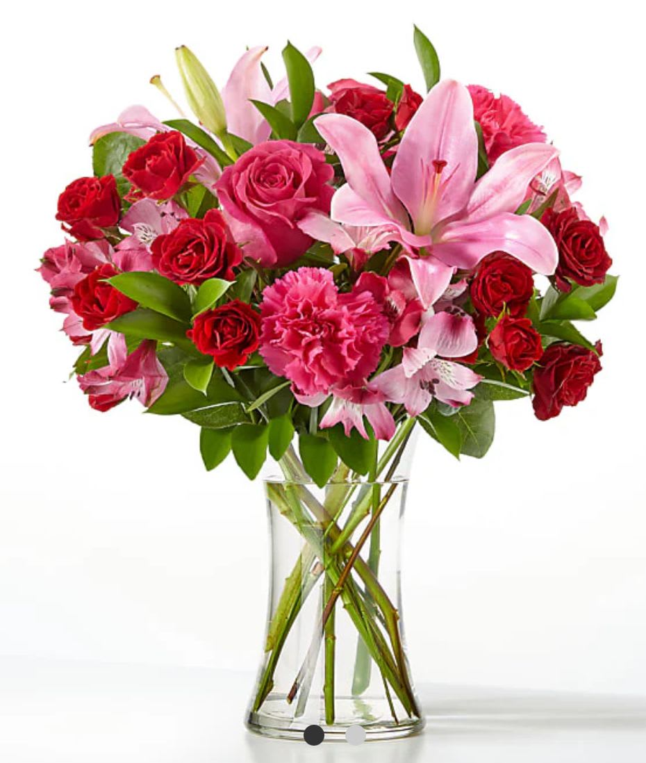 Bouquet of pink lilies, red roses, and carnations in a clear glass vase