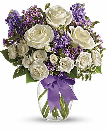 White roses and purple flowers in a clear glass vase with a purple ribbon
