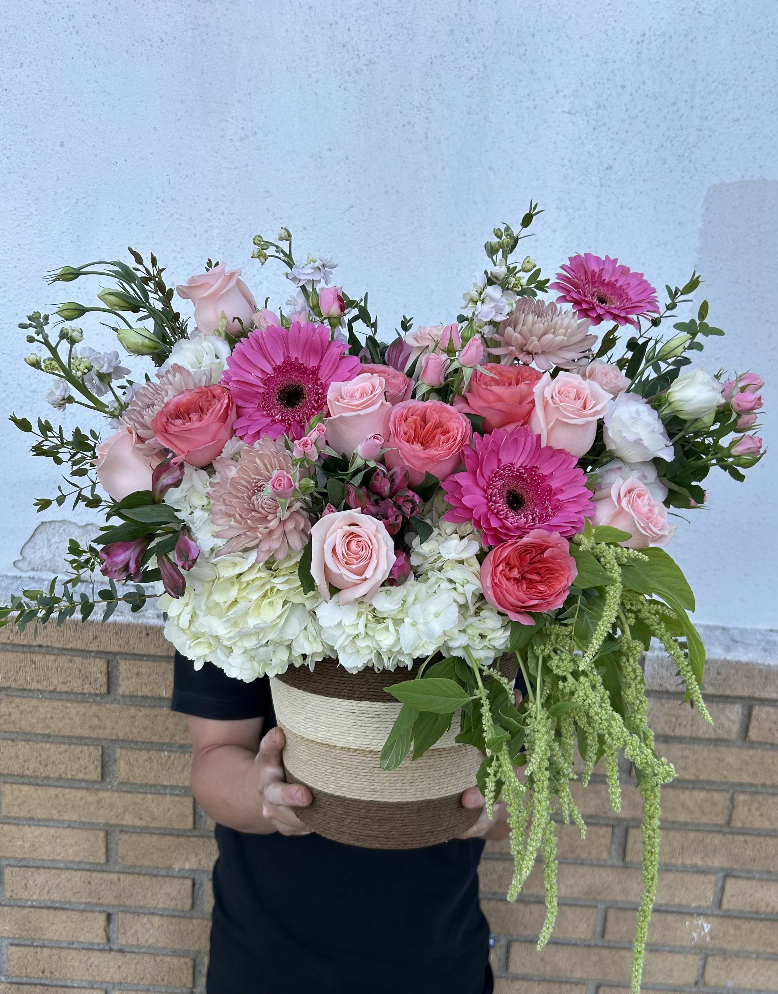 Celebrate Mom with Love - Pink roses, gerbera daisies, hydrangeas and mixed blooms in blush, coral, and white with railing greenery, arranged in a woven basket for a full garden style Mother's Day or celebration gift.