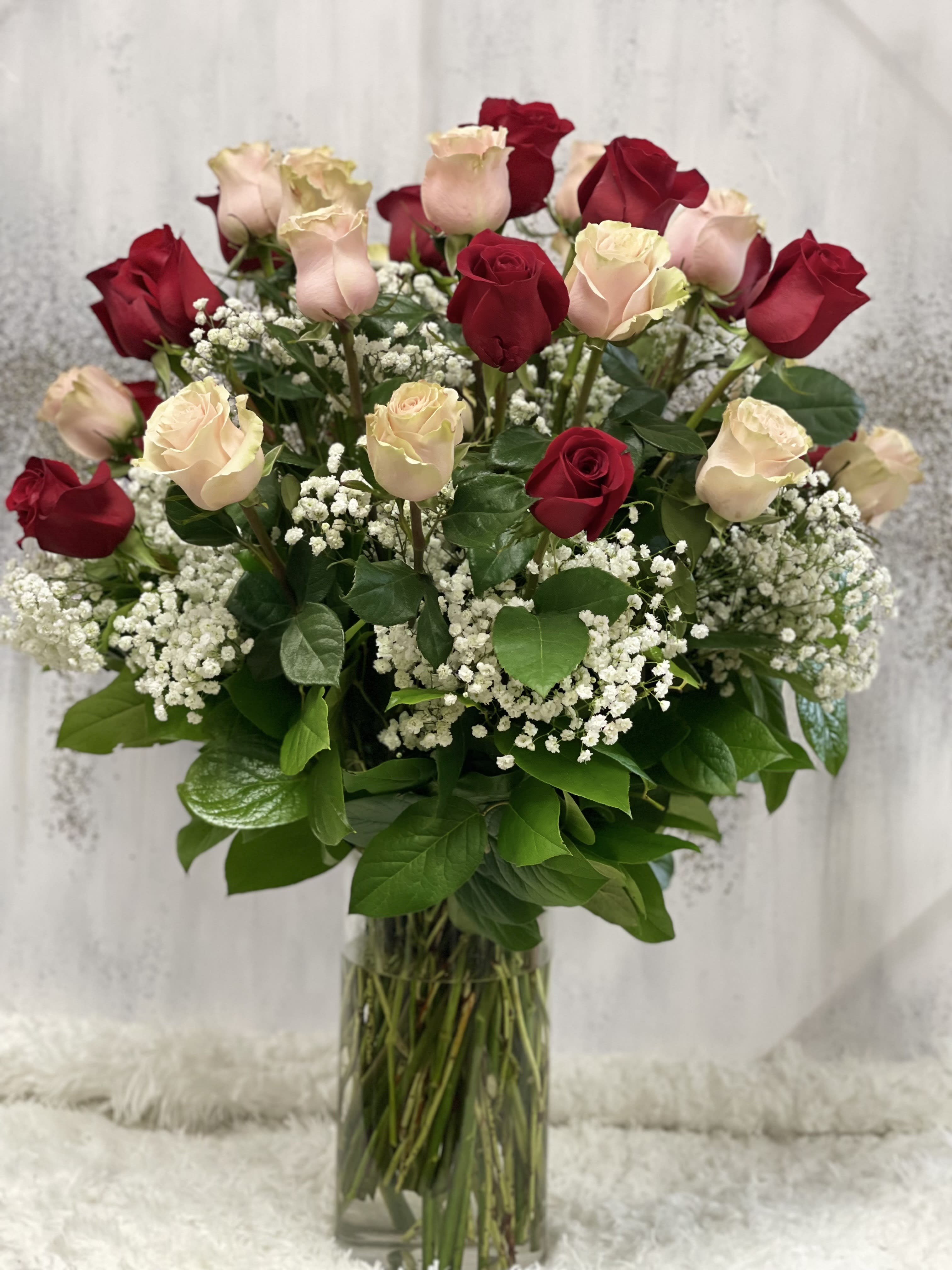 Tall arrangement of red and pale pink roses with white baby's breath in a clear glass vase