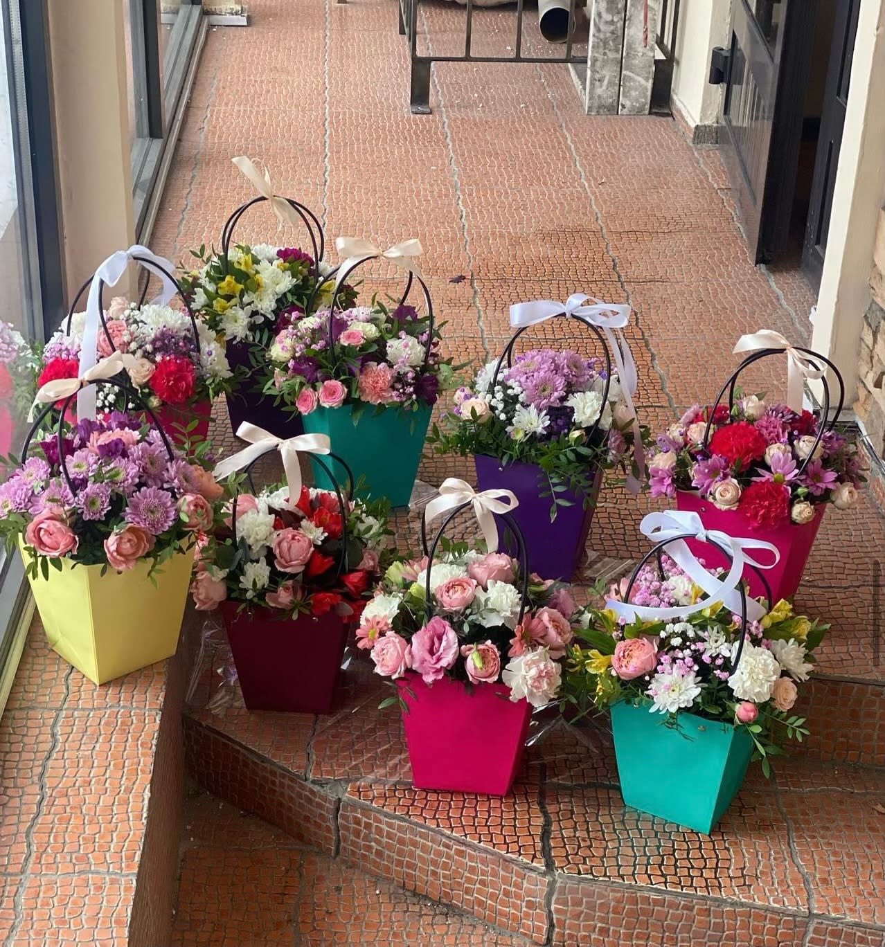 Bright mixed flower arrangements in colorful handled gift boxes with ribbon bows on outdoor steps