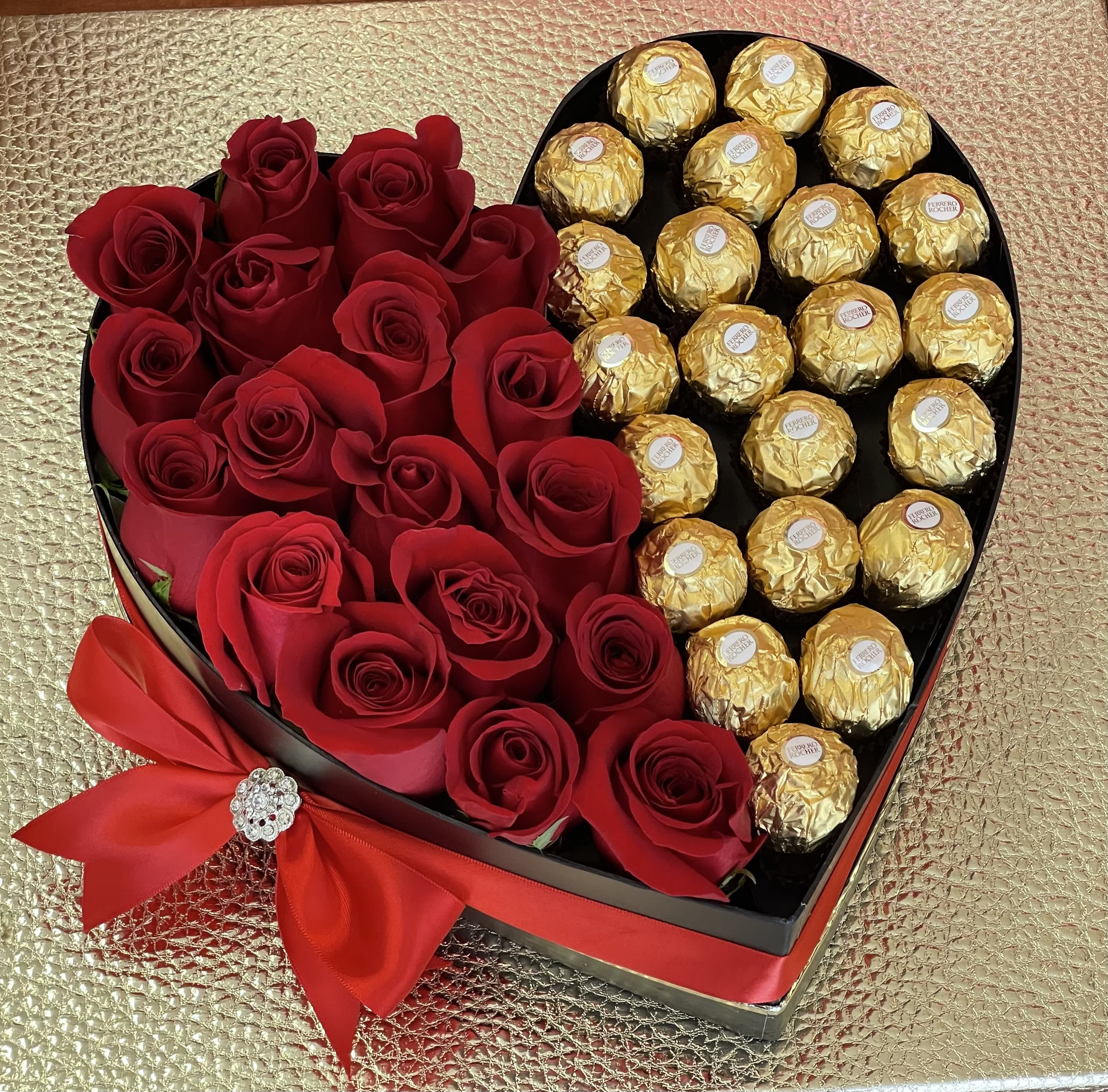 Heart-shaped box filled with red roses and gold-wrapped chocolates, tied with a red bow.