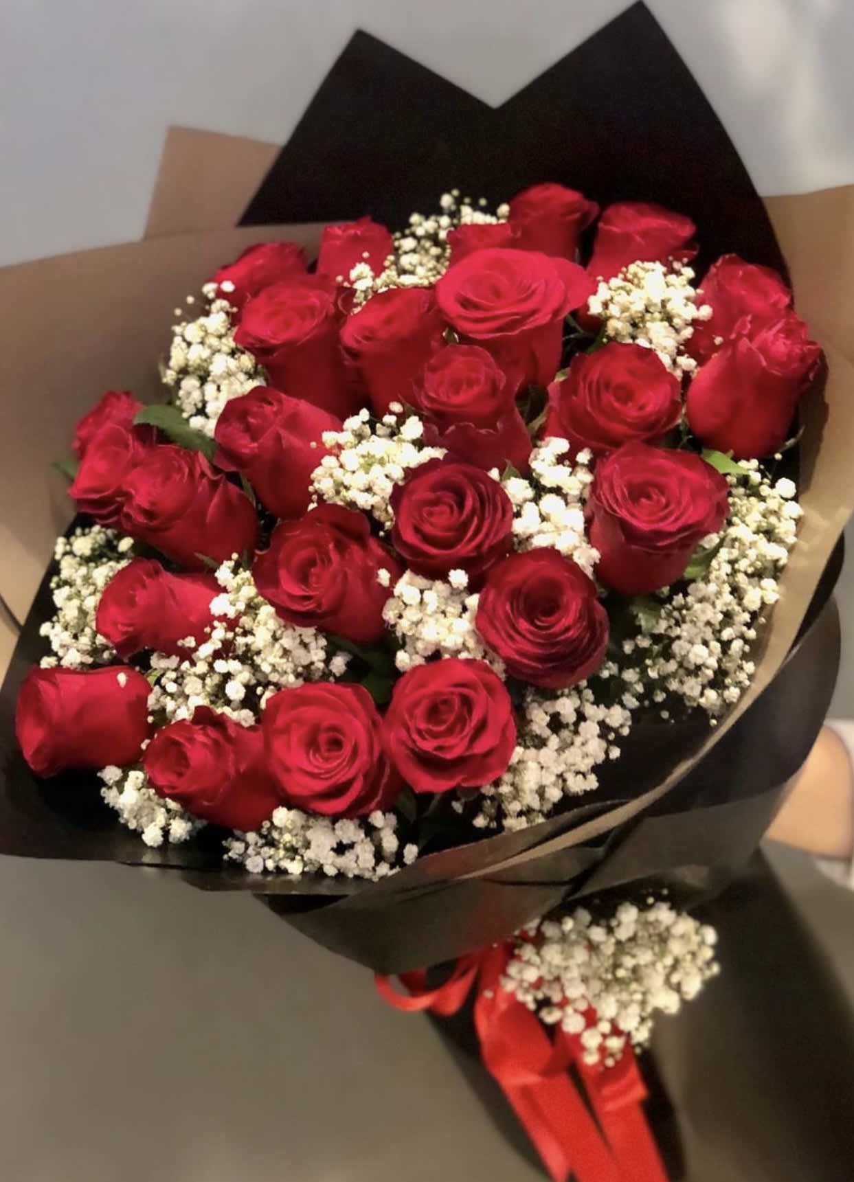 Hand-tied bouquet of red roses with white filler flowers wrapped in black and kraft paper