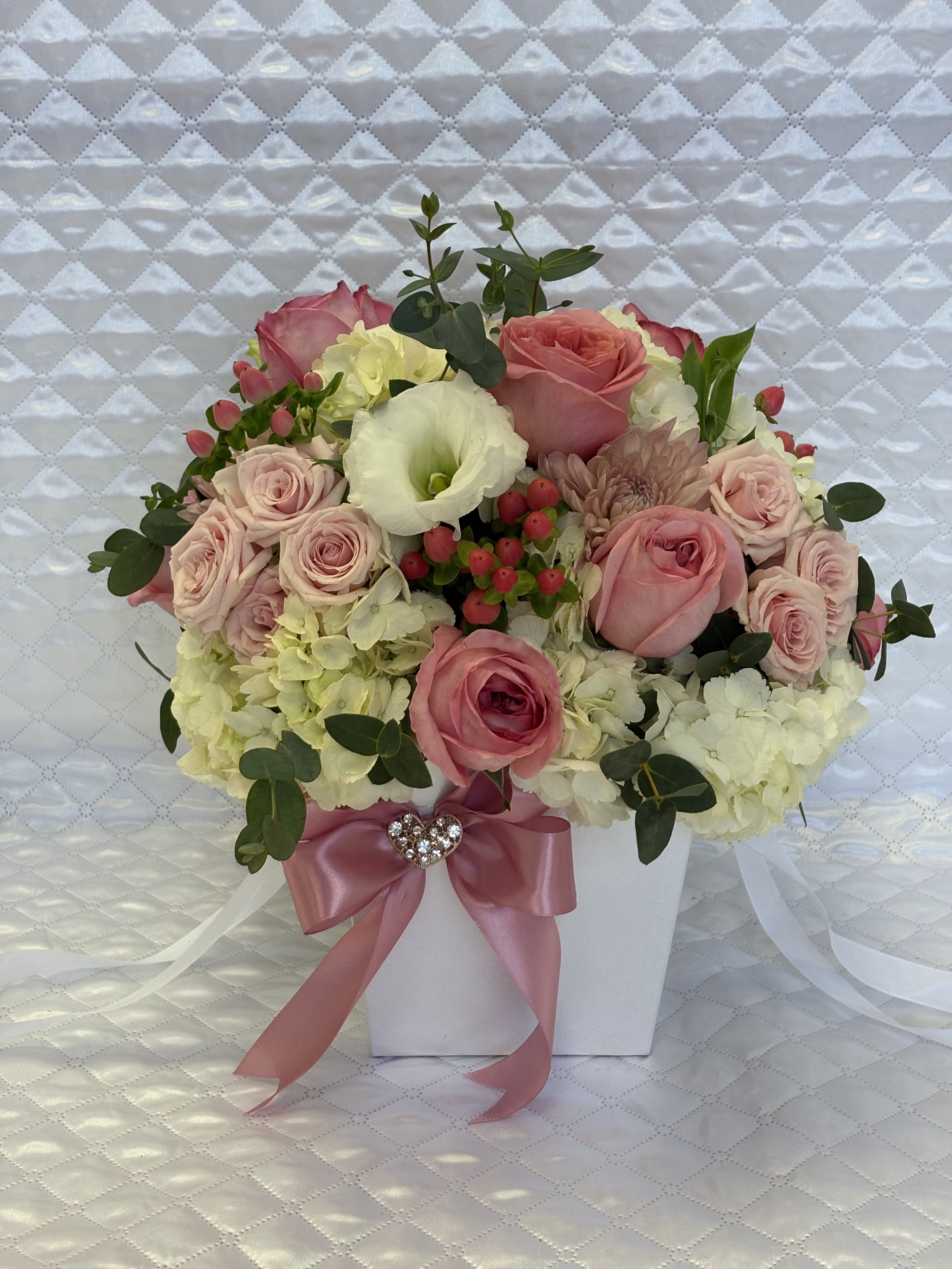 Pink roses and white hydrangeas arranged in a white box with a pink ribbon