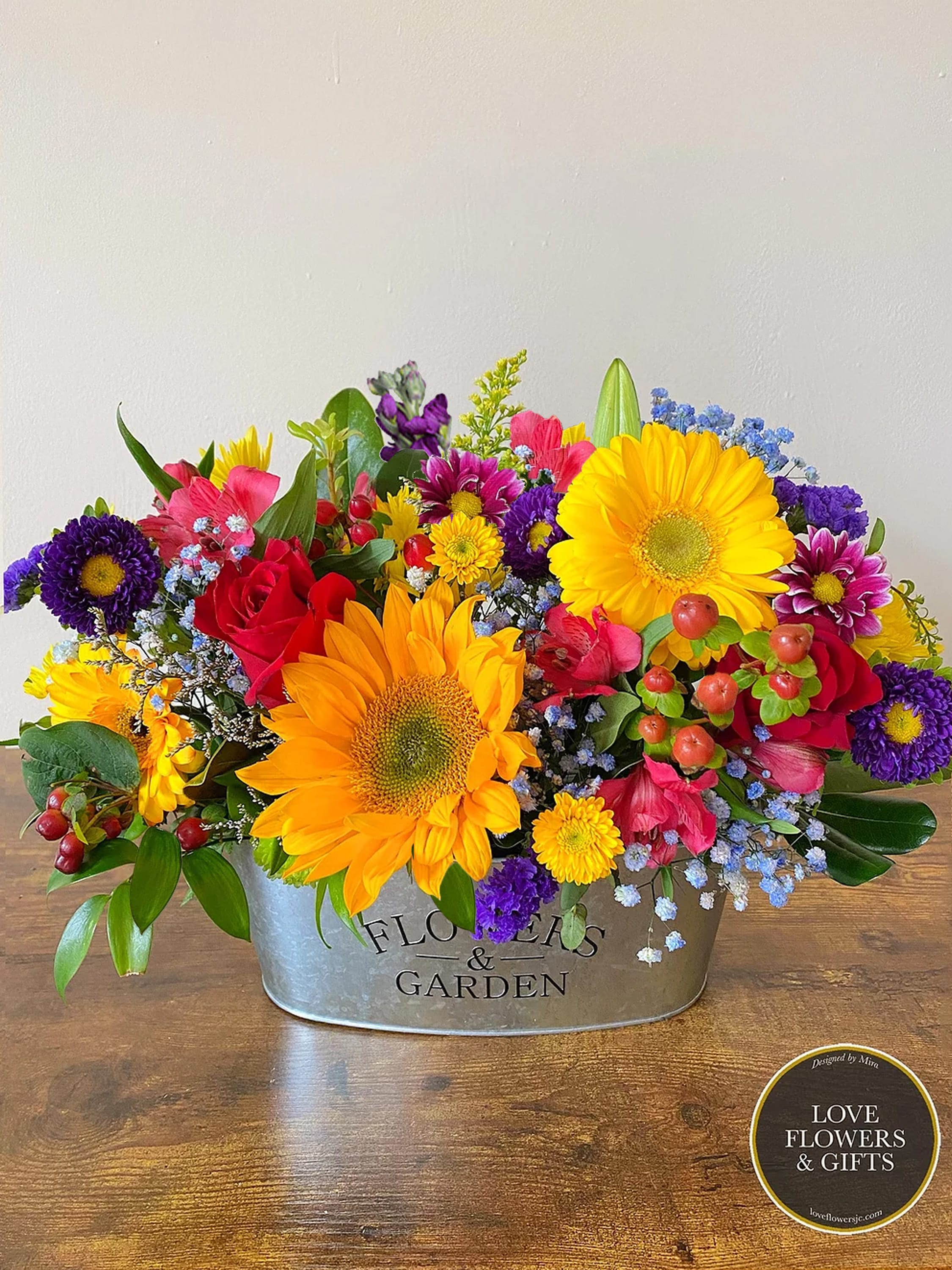 Low galvanized tin arrangement of bright sunflowers, red roses, and mixed colorful blooms