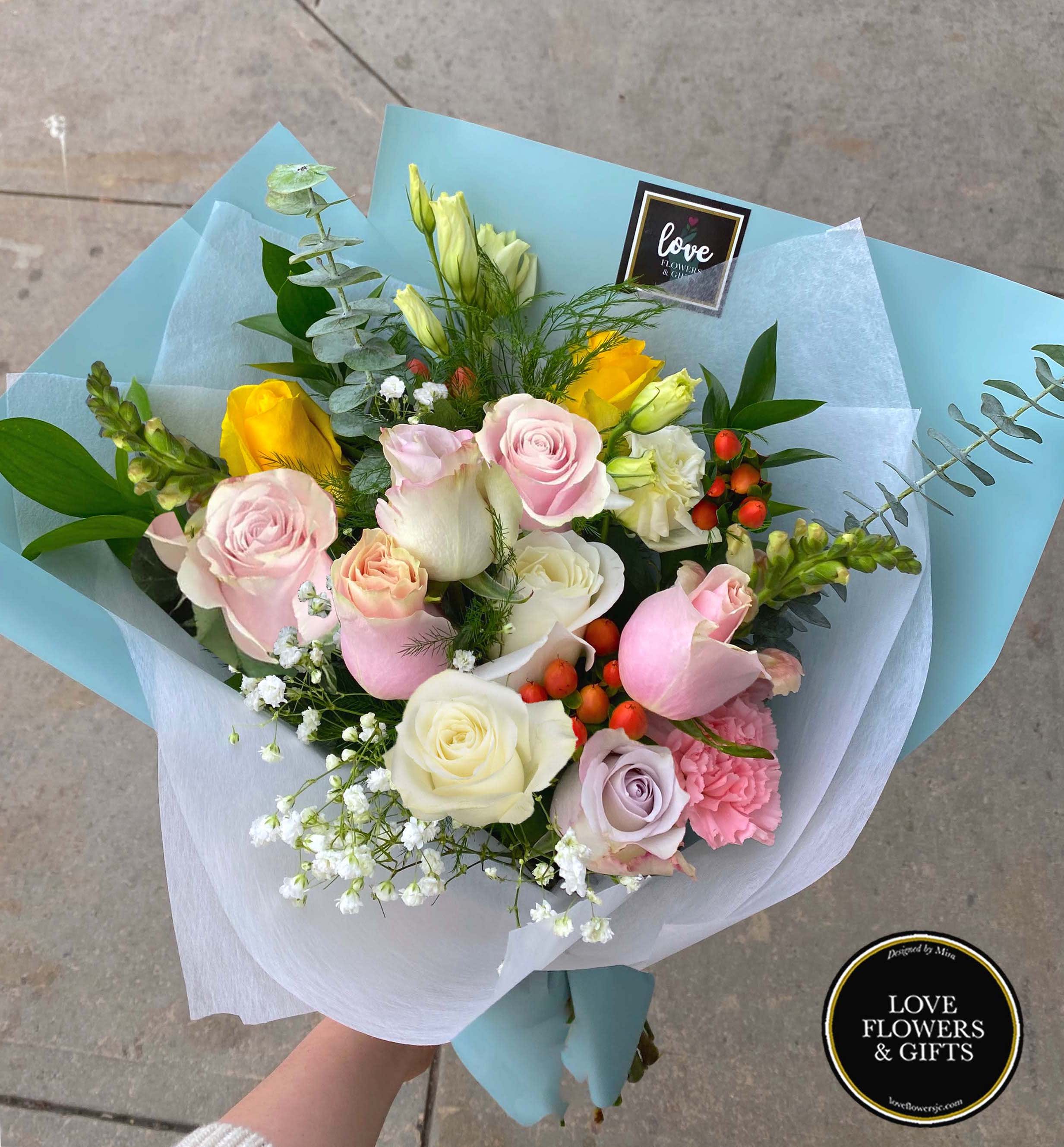 Hand-tied bouquet of pastel roses and mixed flowers wrapped in light blue paper