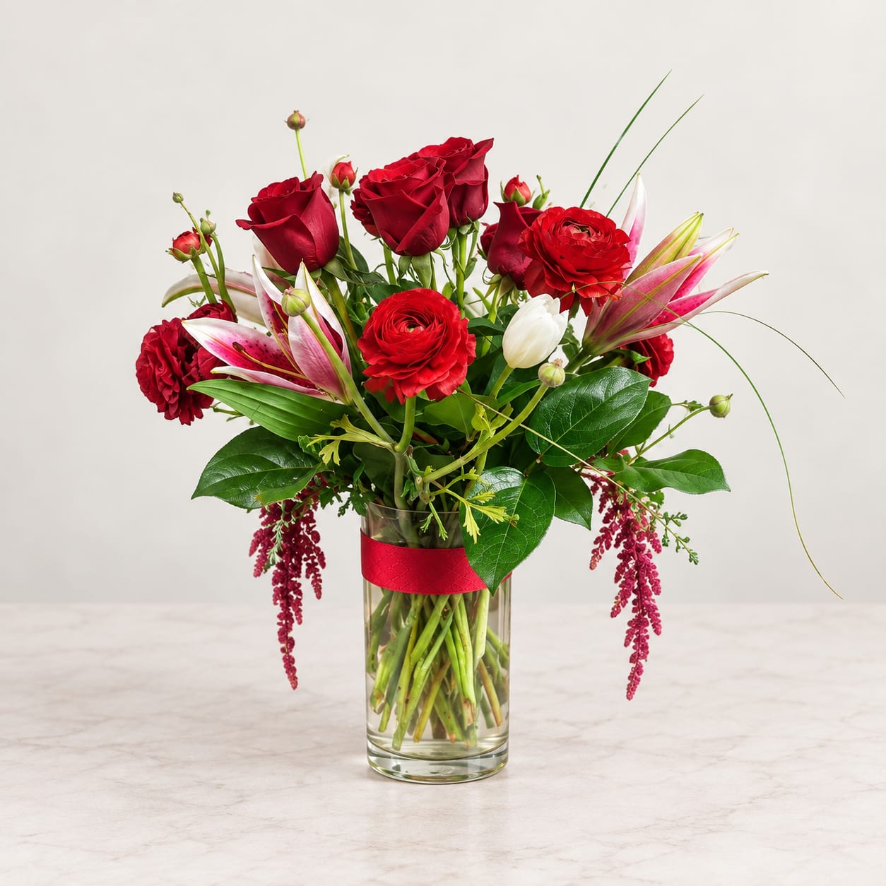 Red roses and lilies arranged in a clear glass vase with a red ribbon