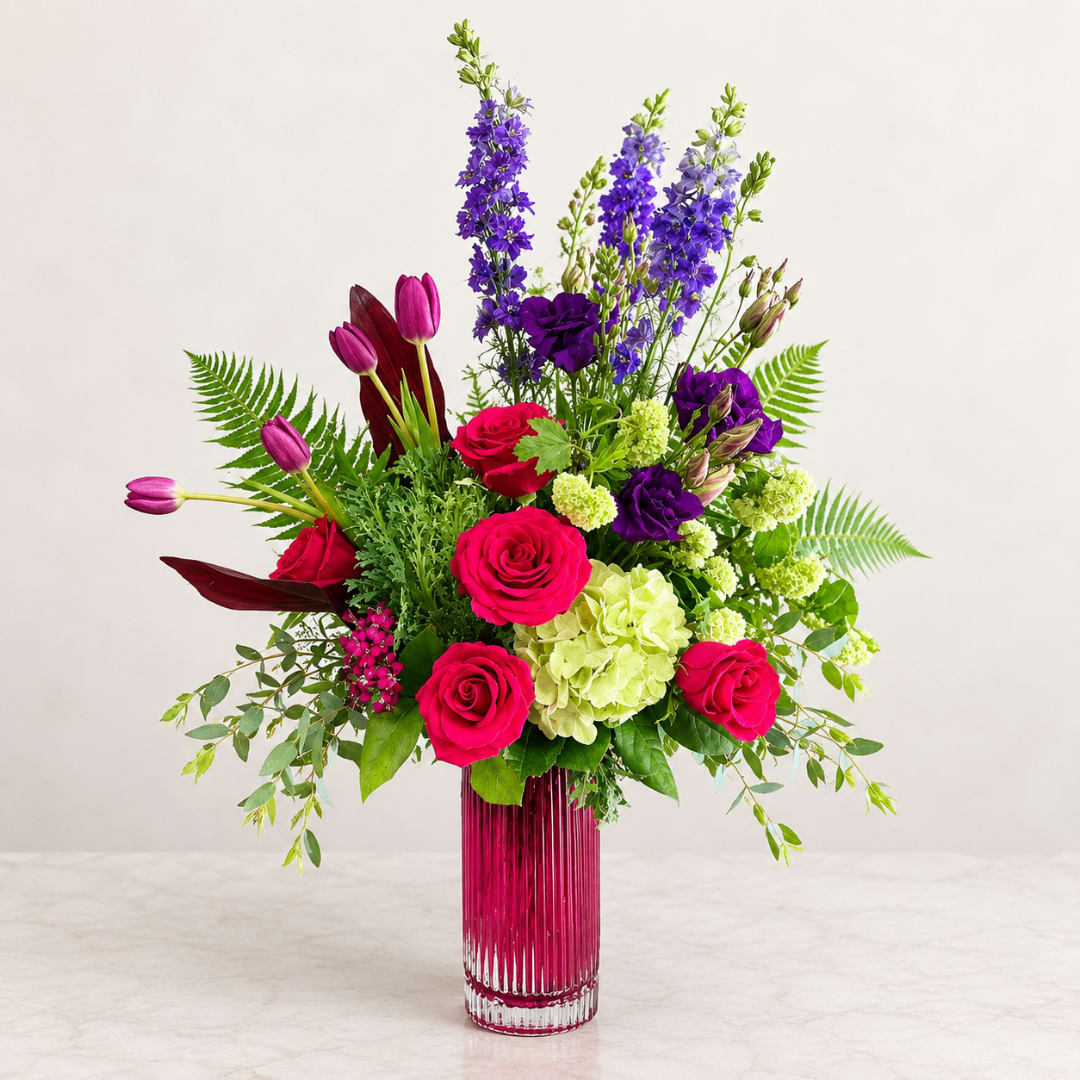 Mixed bouquet of pink roses, purple blooms, and green hydrangea in a tall glass vase