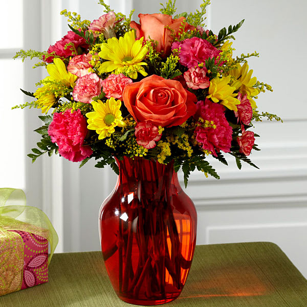 The FTD Colors Abound Bouquet - Full of energy and light to help you celebrate with friends and family near and far this stunning fresh flower arrangement is that perfect gift. Orange roses yellow daisies hot pink carnations orange mini carnations yellow solidago and lush greens are arranged beautifully in an eye-catching orange glass vase. A fun way to surprise and delight your recipient in honor of a birthday or to offer your congratulations wishes! 