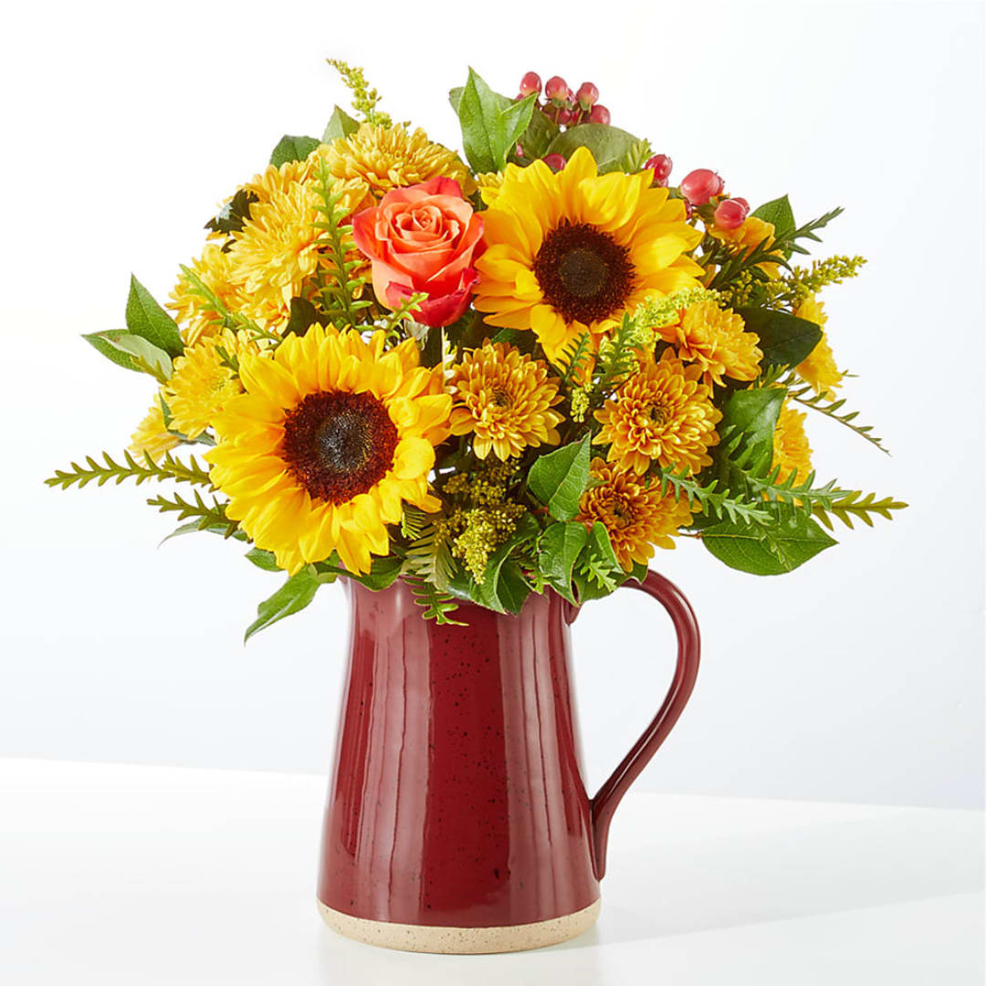 Sunflowers and orange roses arranged in a red pitcher vase