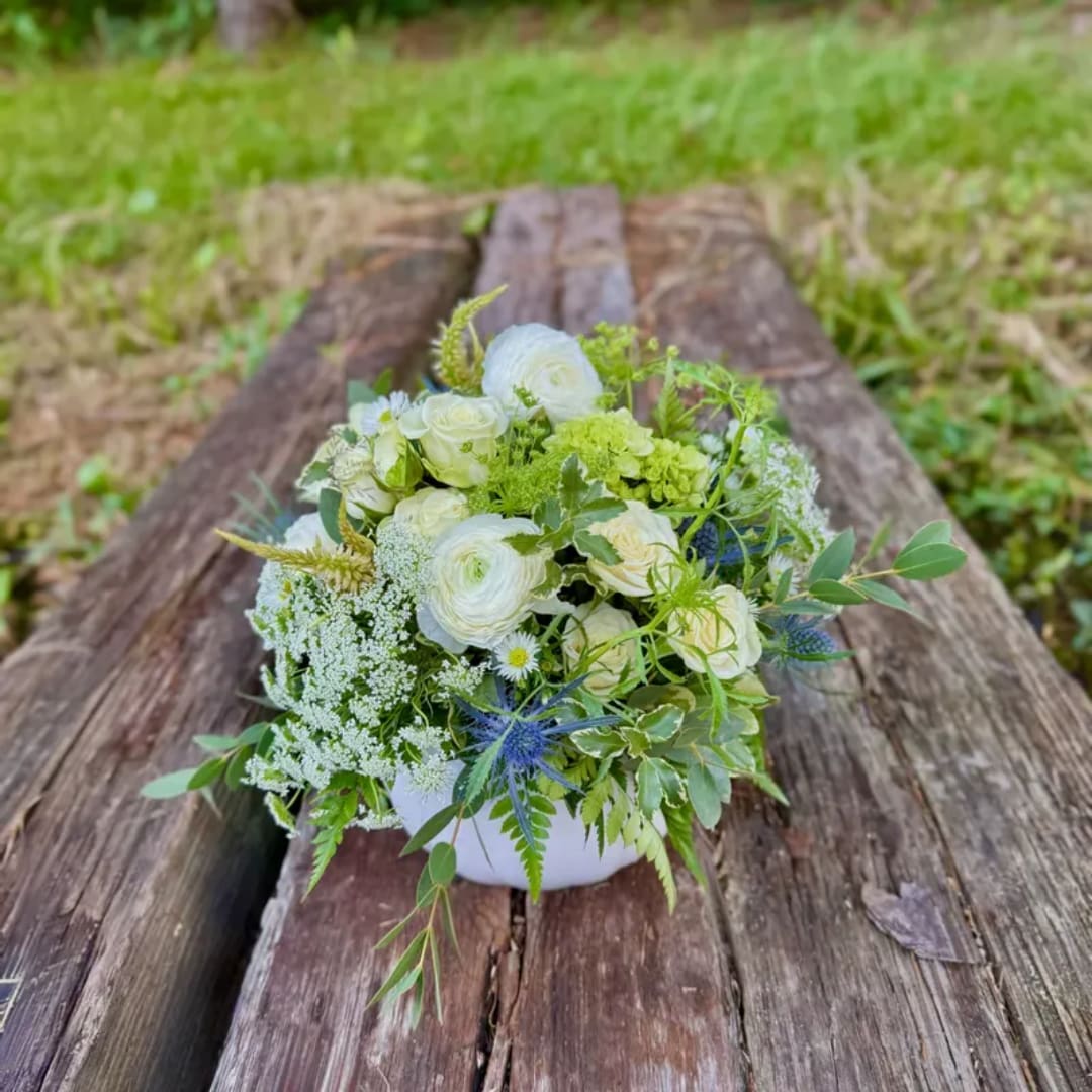 White and green floral arrangement in a low white bowl on weathered wood