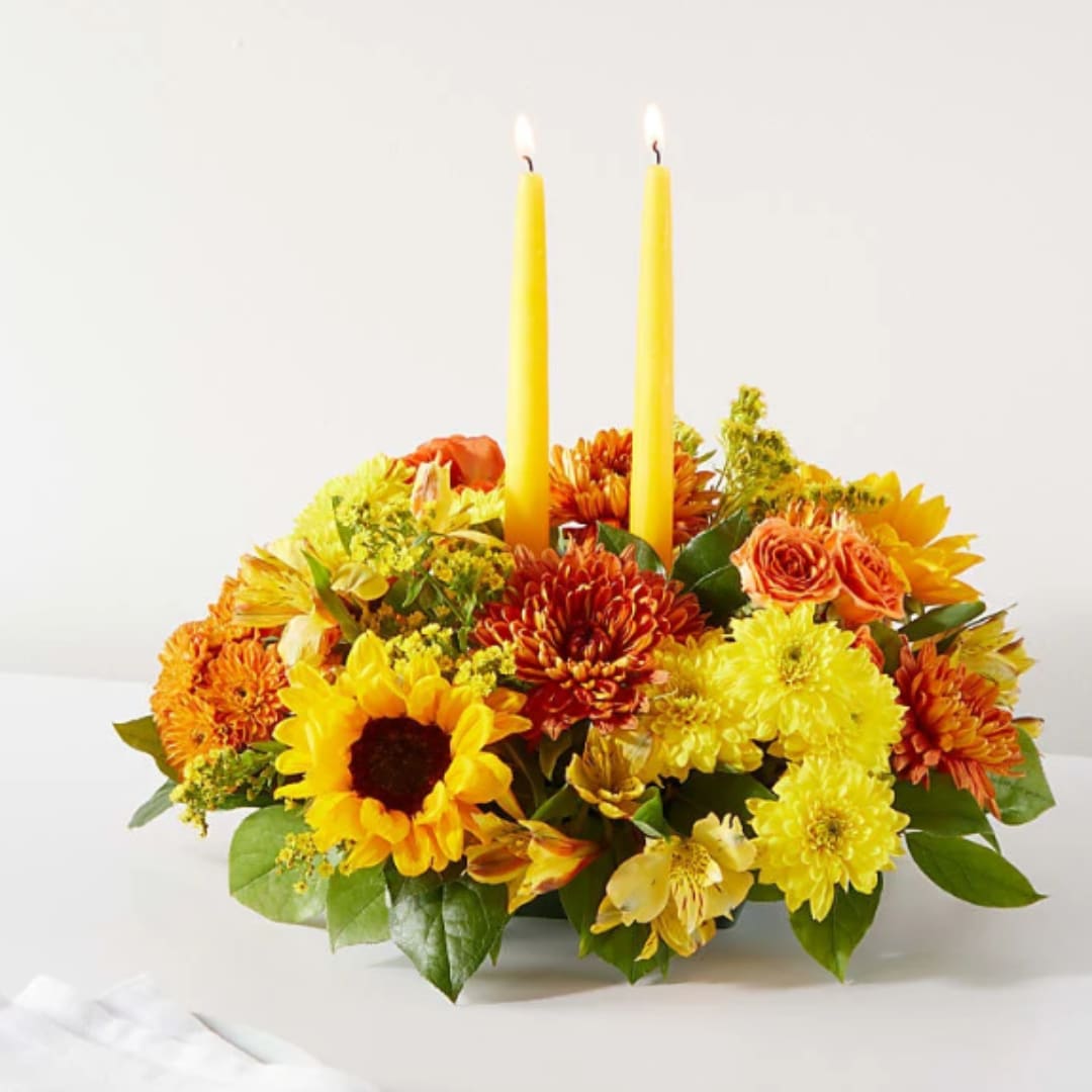 Yellow and orange floral centerpiece with two lit taper candles