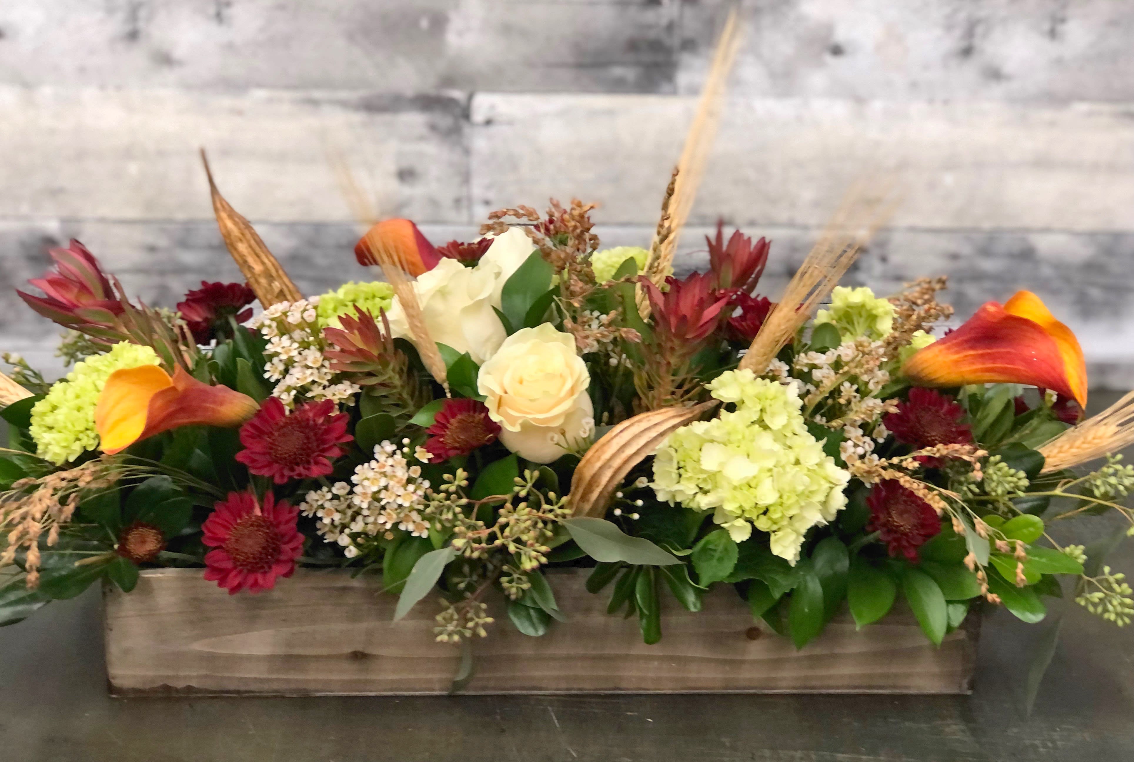 Autumn Grace - Rustic yet elegant, this unique centerpiece has loads of bright fall colors and textures with a classic hurricane and pillar candle all arranged in a vintage box!  Approximately 26” x 14” x 10”. Don’t want a candle? No problem, just leave a note in the special instructions section of your order and we will add more flowers instead!