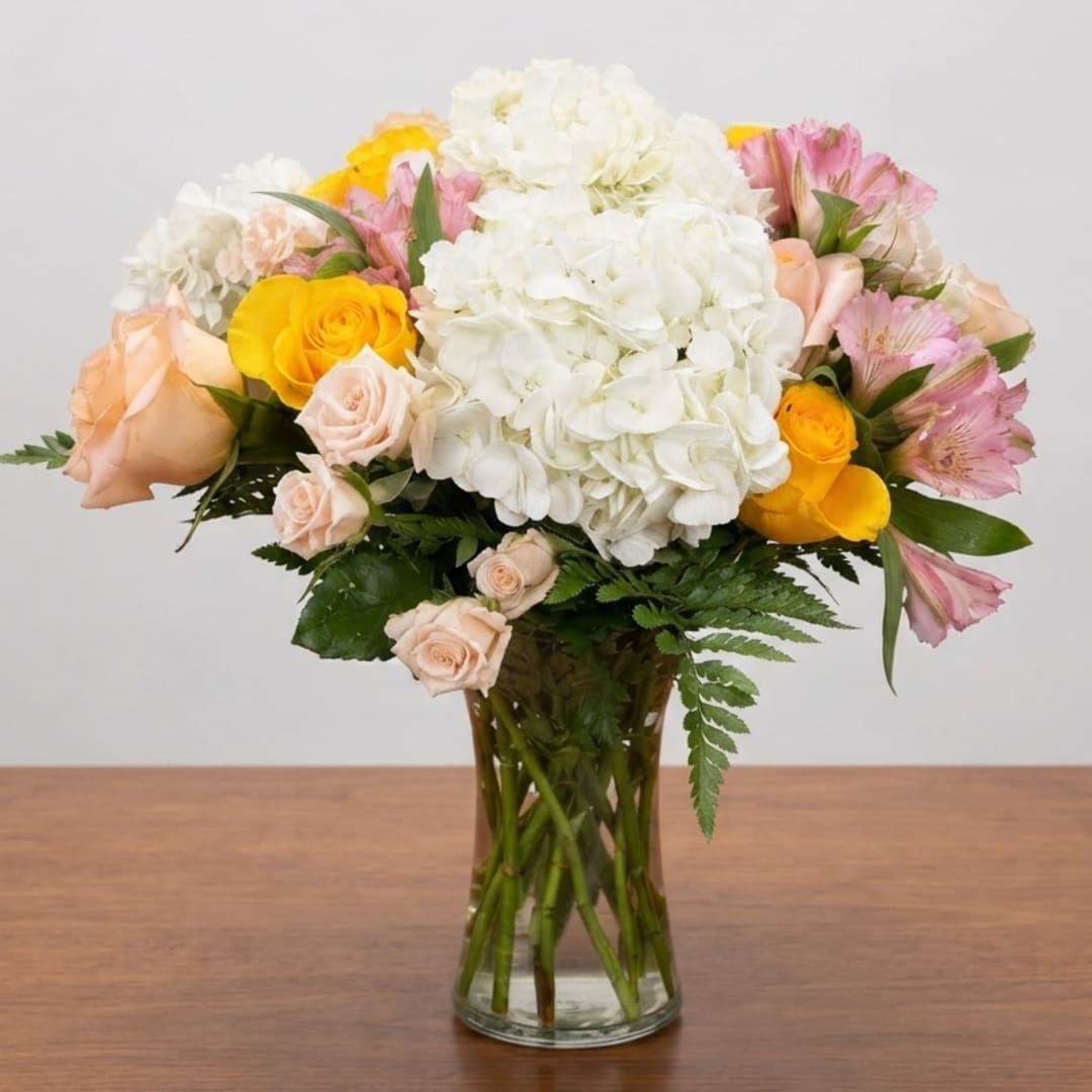 Bouquet of white hydrangeas, yellow and peach roses, and pink alstroemeria in a glass vase