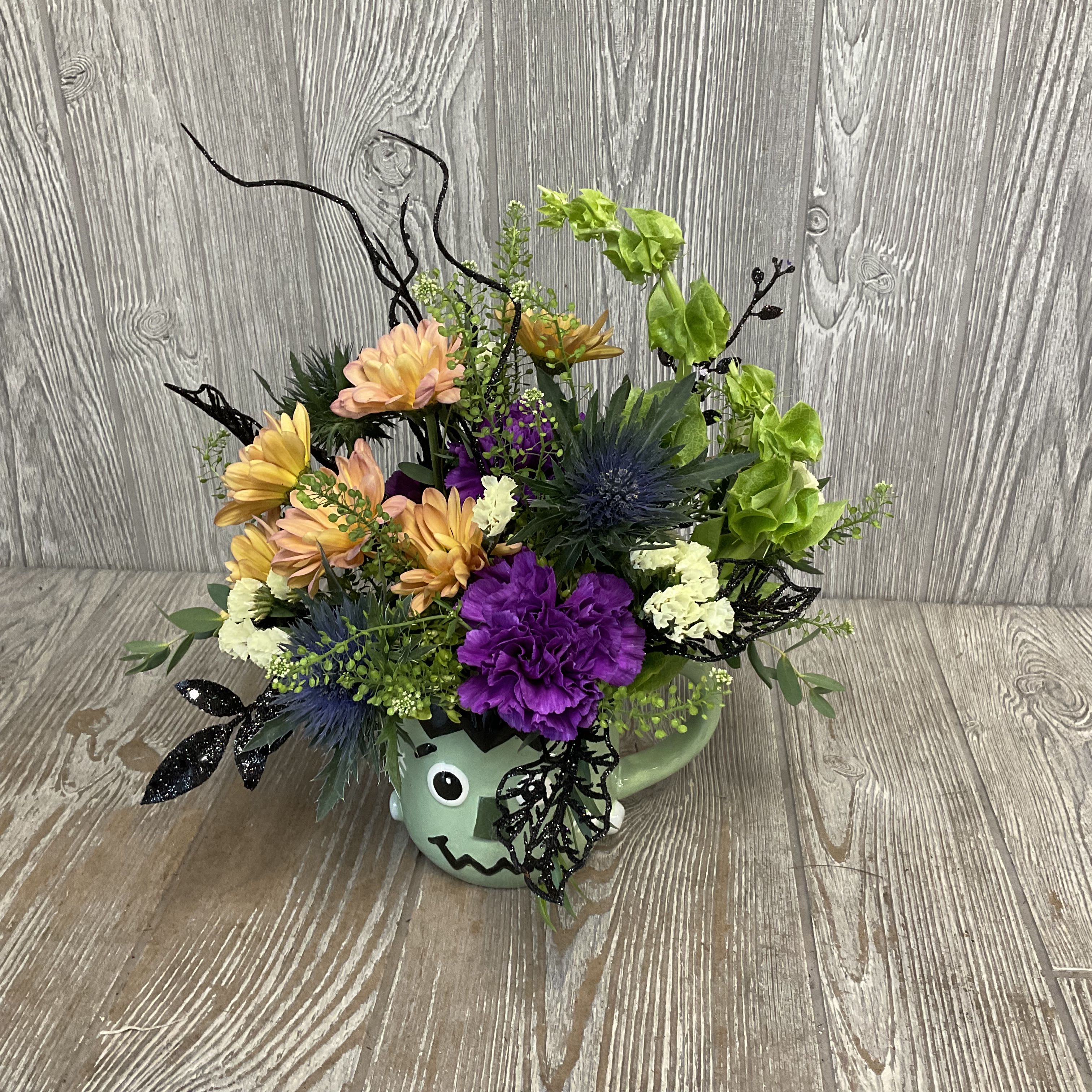 Colorful floral arrangement in a green monster mug with black decorative accents